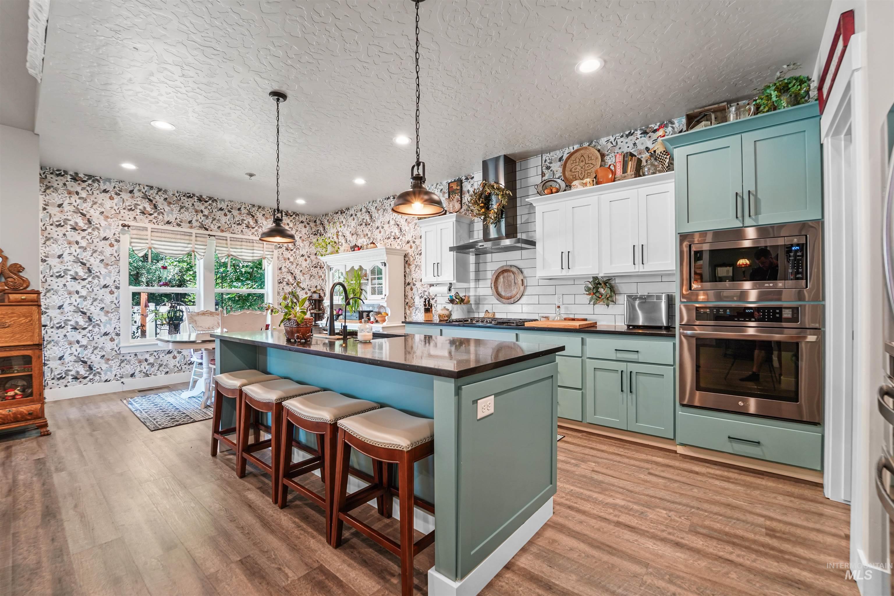 Kitchen featuring green cabinetry, wallpapered walls, recessed lighting, a textured ceiling, and stainless steel appliances