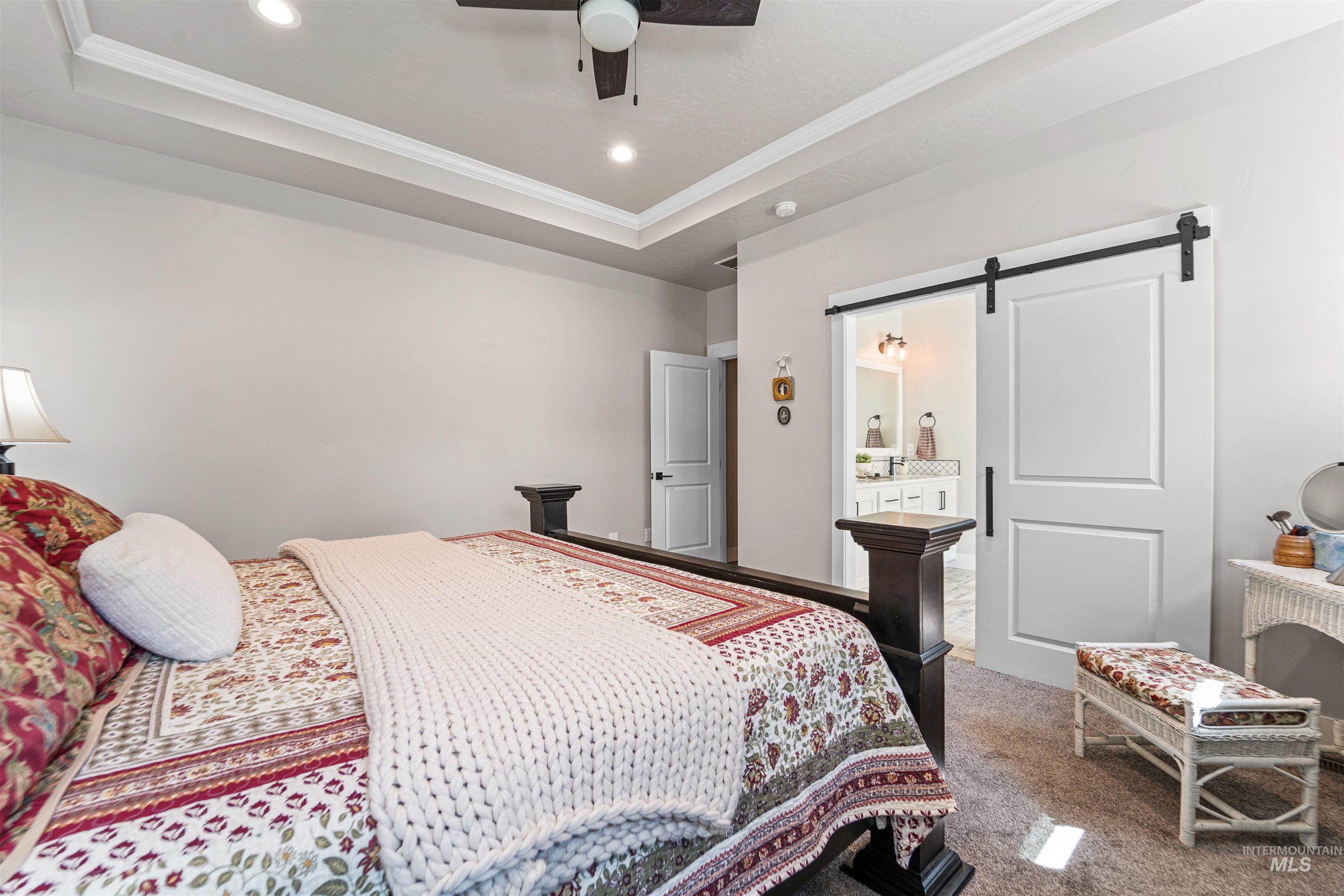 Bedroom with a barn door, a raised ceiling, carpet flooring, ceiling fan, and ornamental molding