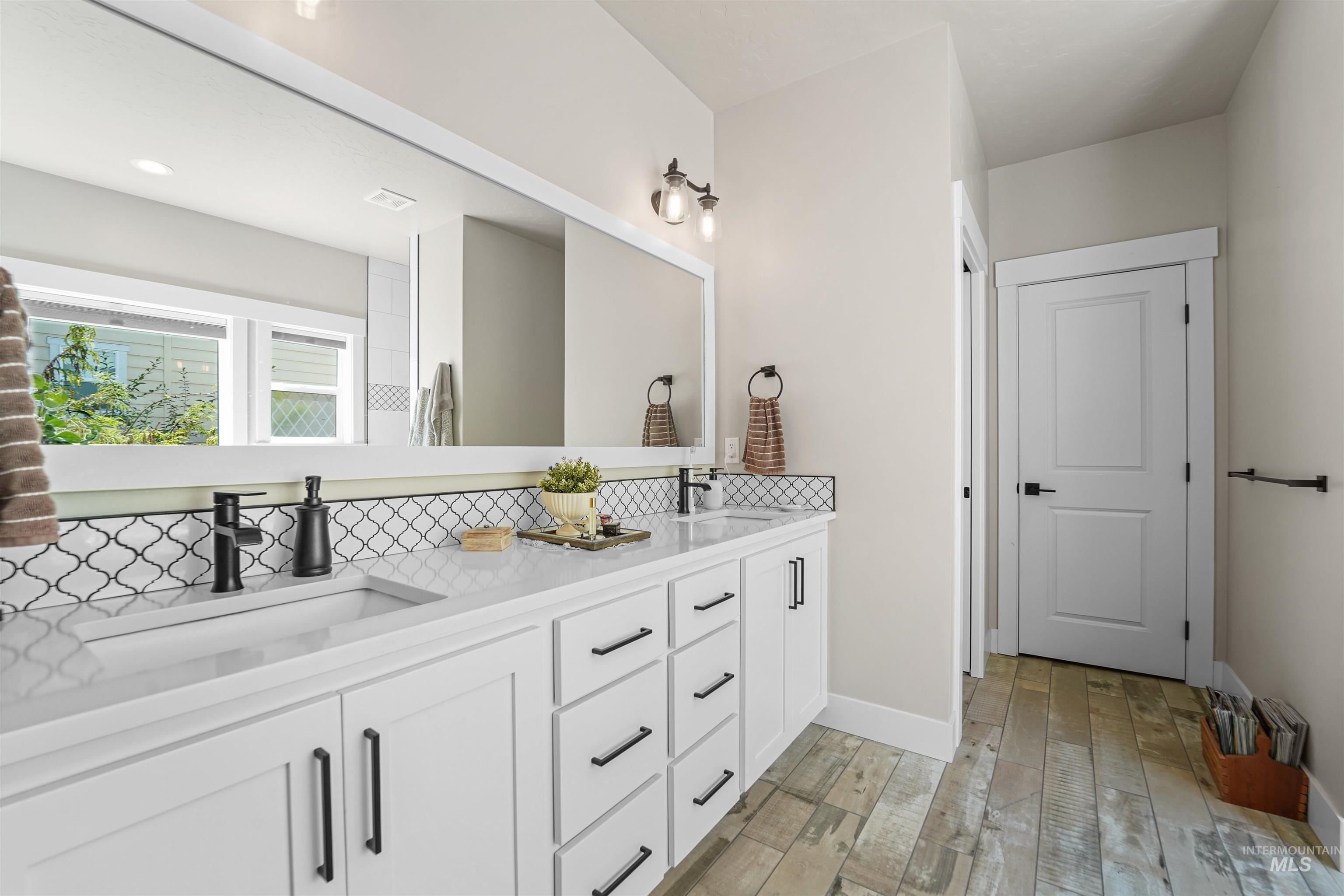 Bathroom with double vanity, light wood-style floors, and decorative backsplash