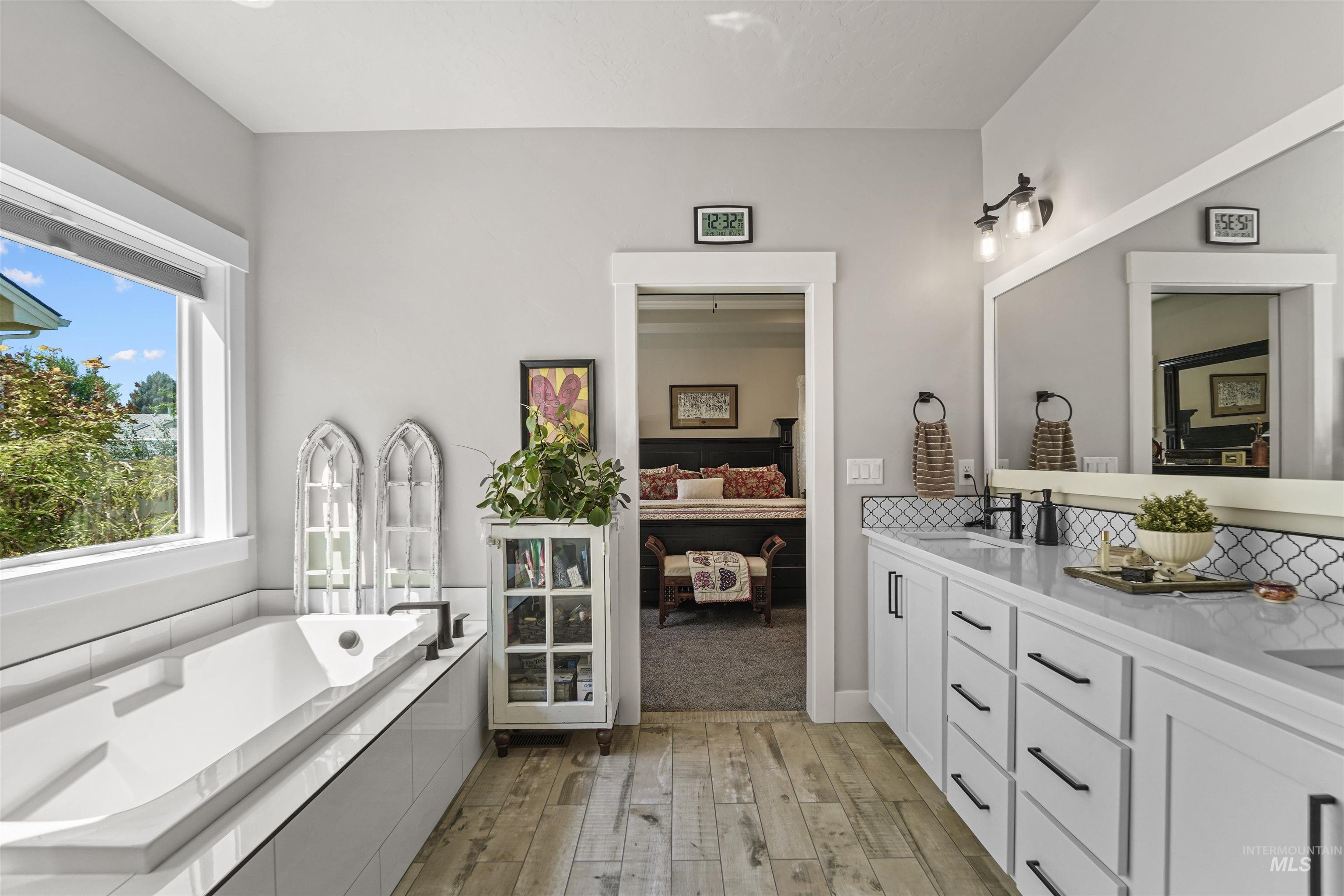 Ensuite bathroom with double vanity, light wood finished floors, and a bath
