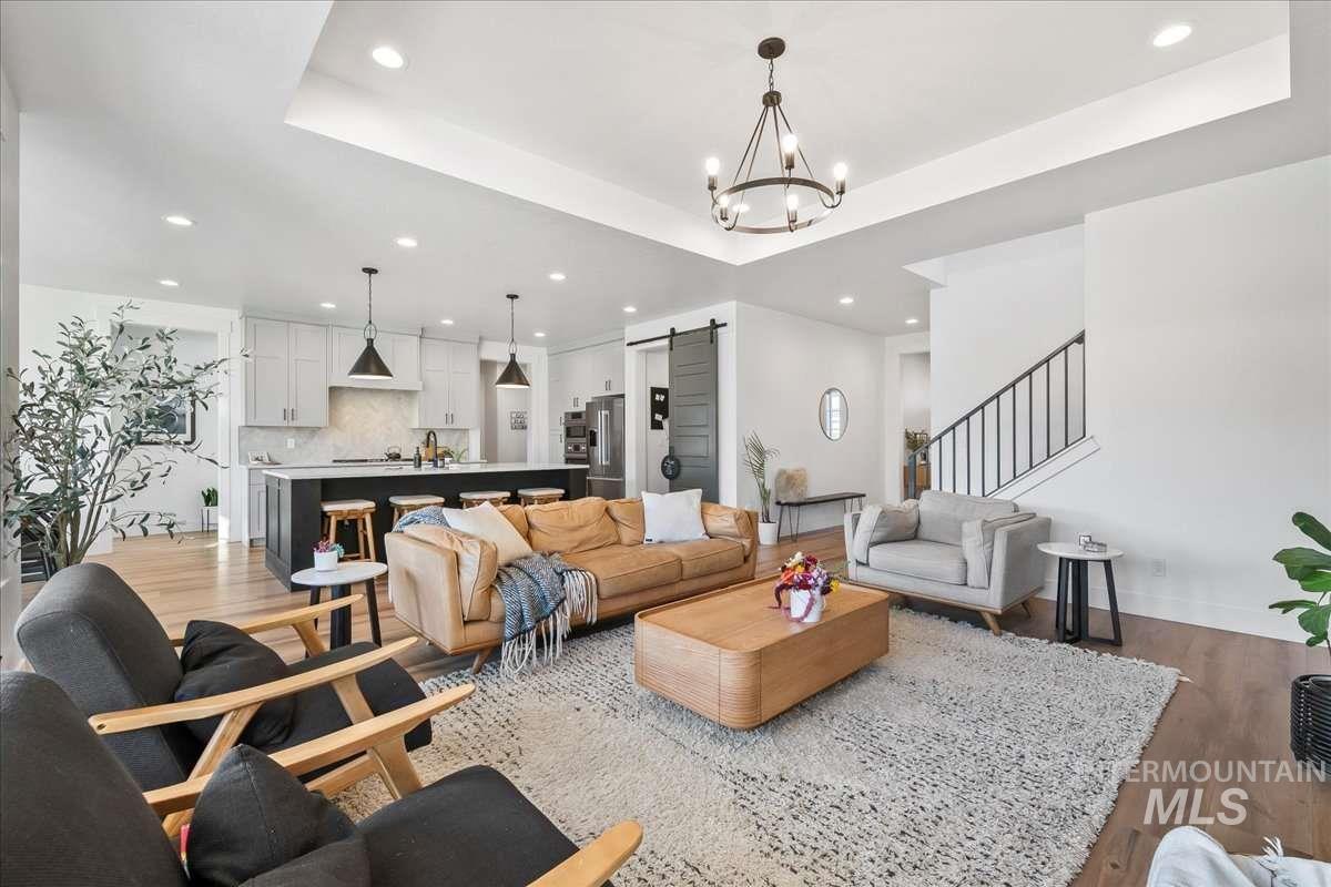 Living room featuring a barn door, light wood-style flooring, a tray ceiling, recessed lighting, and stairs
