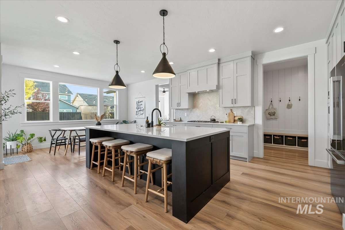 Kitchen with backsplash, a breakfast bar, pendant lighting, an island with sink, and light wood-style floors