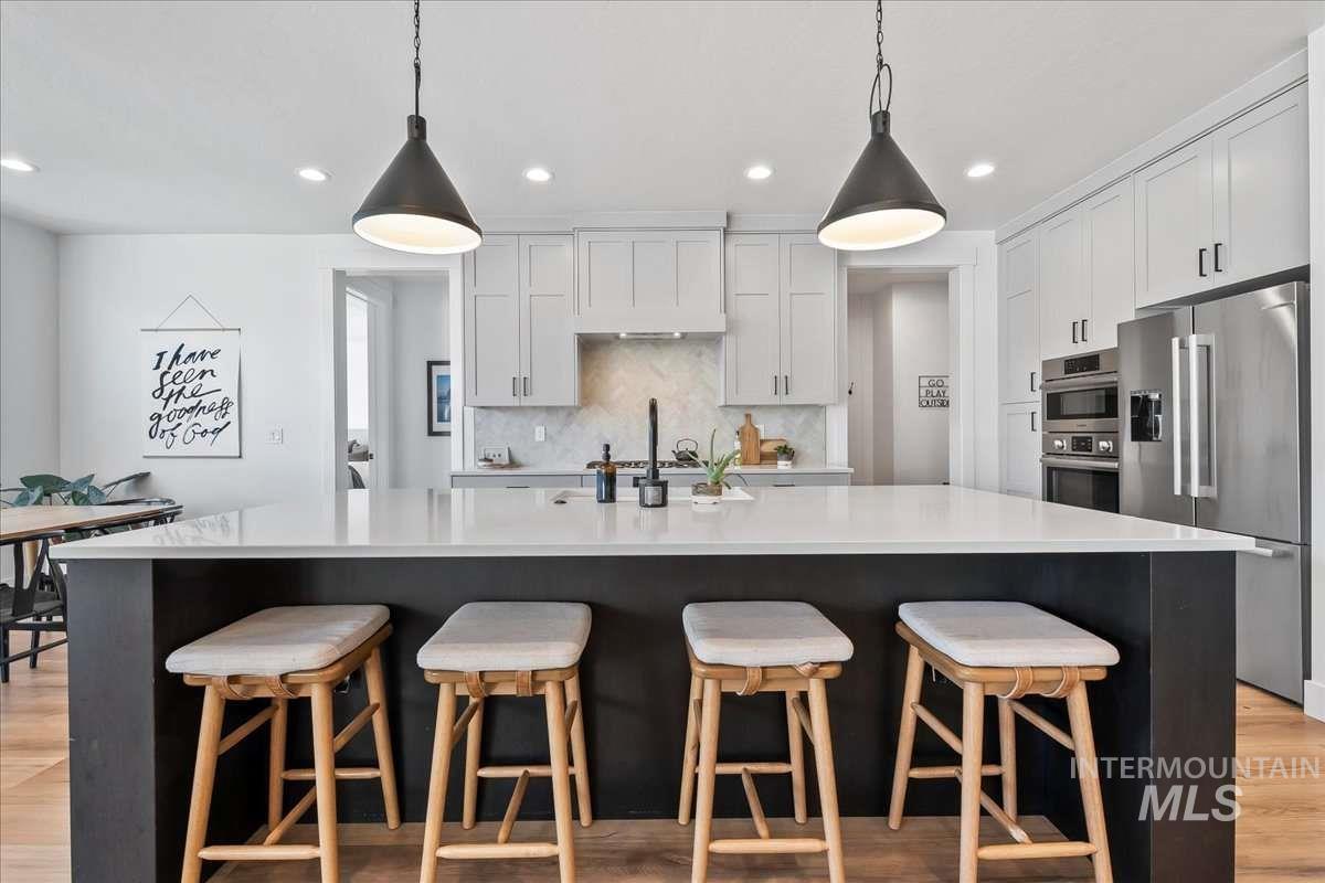 Kitchen with appliances with stainless steel finishes, light wood-style floors, tasteful backsplash, recessed lighting, and white cabinetry