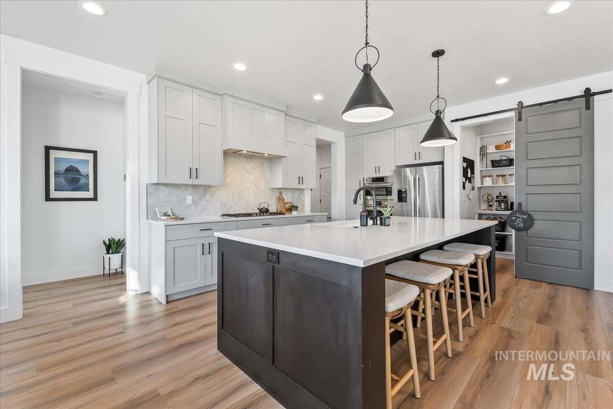 Kitchen with a barn door, a kitchen island with sink, tasteful backsplash, a breakfast bar area, and pendant lighting