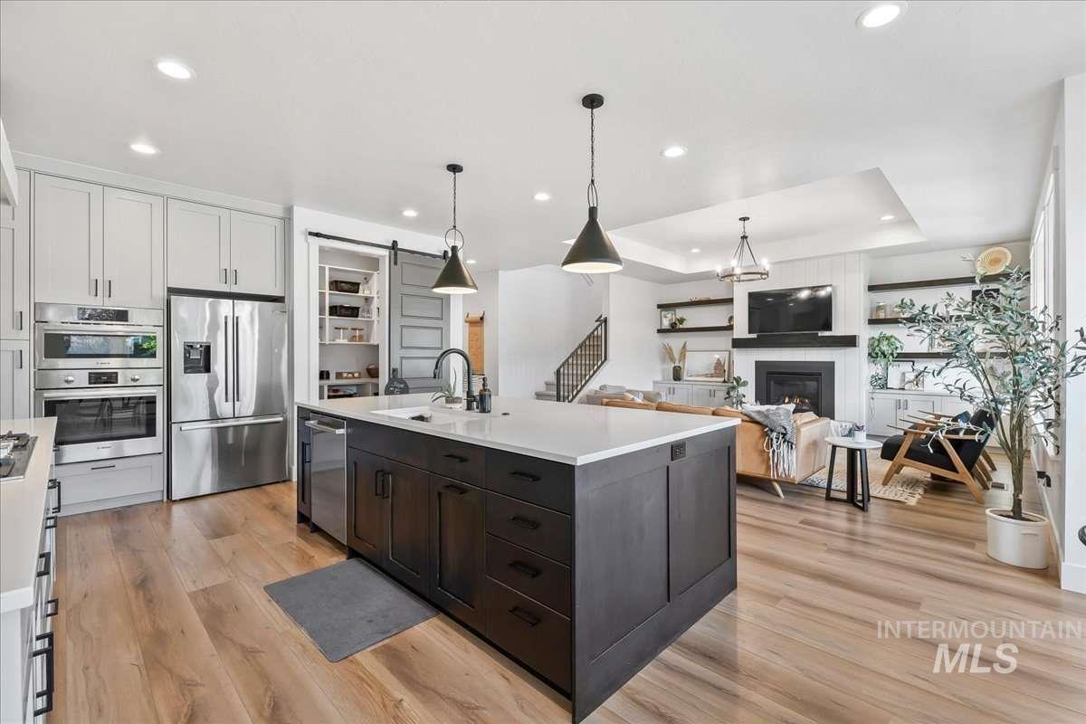 Kitchen with a barn door, appliances with stainless steel finishes, a raised ceiling, open floor plan, and hanging light fixtures