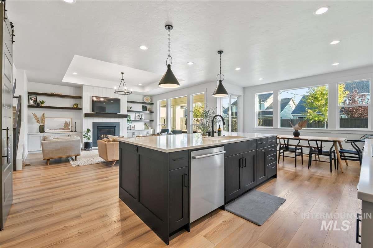 Kitchen with dark cabinetry, hanging light fixtures, a glass covered fireplace, light wood-style flooring, and recessed lighting