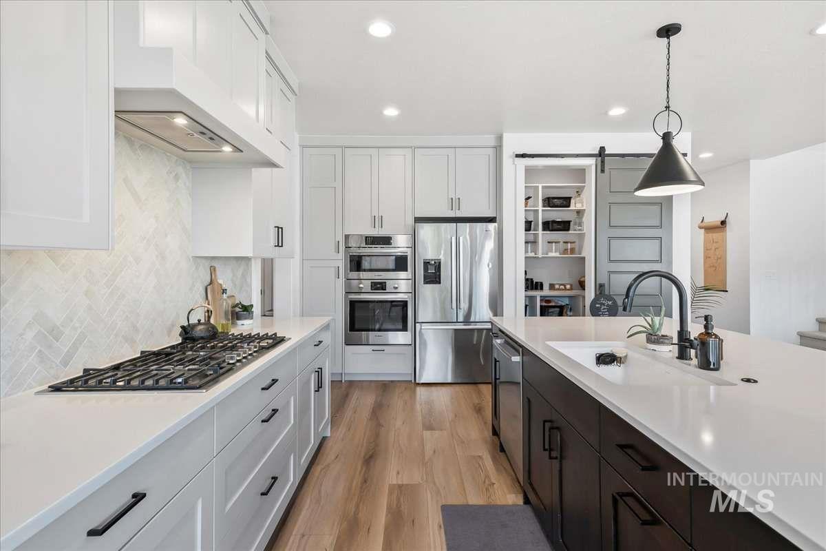 Kitchen featuring appliances with stainless steel finishes, white cabinetry, light wood finished floors, a barn door, and custom exhaust hood