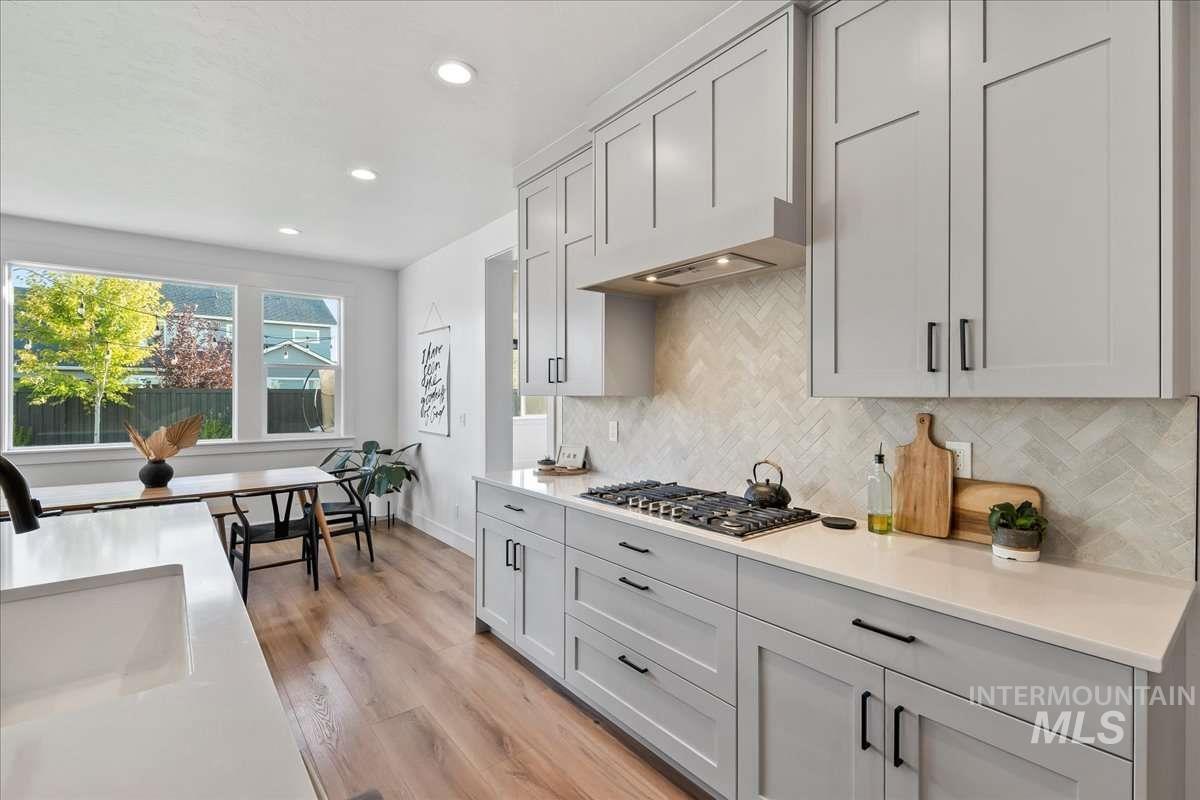 Kitchen with light wood-style floors, tasteful backsplash, recessed lighting, stainless steel gas cooktop, and light stone counters