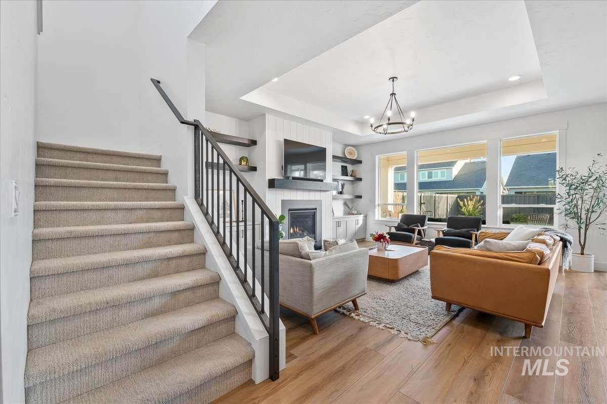 Living room with a tray ceiling, stairs, a glass covered fireplace, and light wood-style flooring