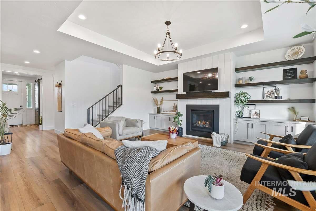 Living area featuring a tray ceiling, wood finished floors, recessed lighting, a large fireplace, and stairway