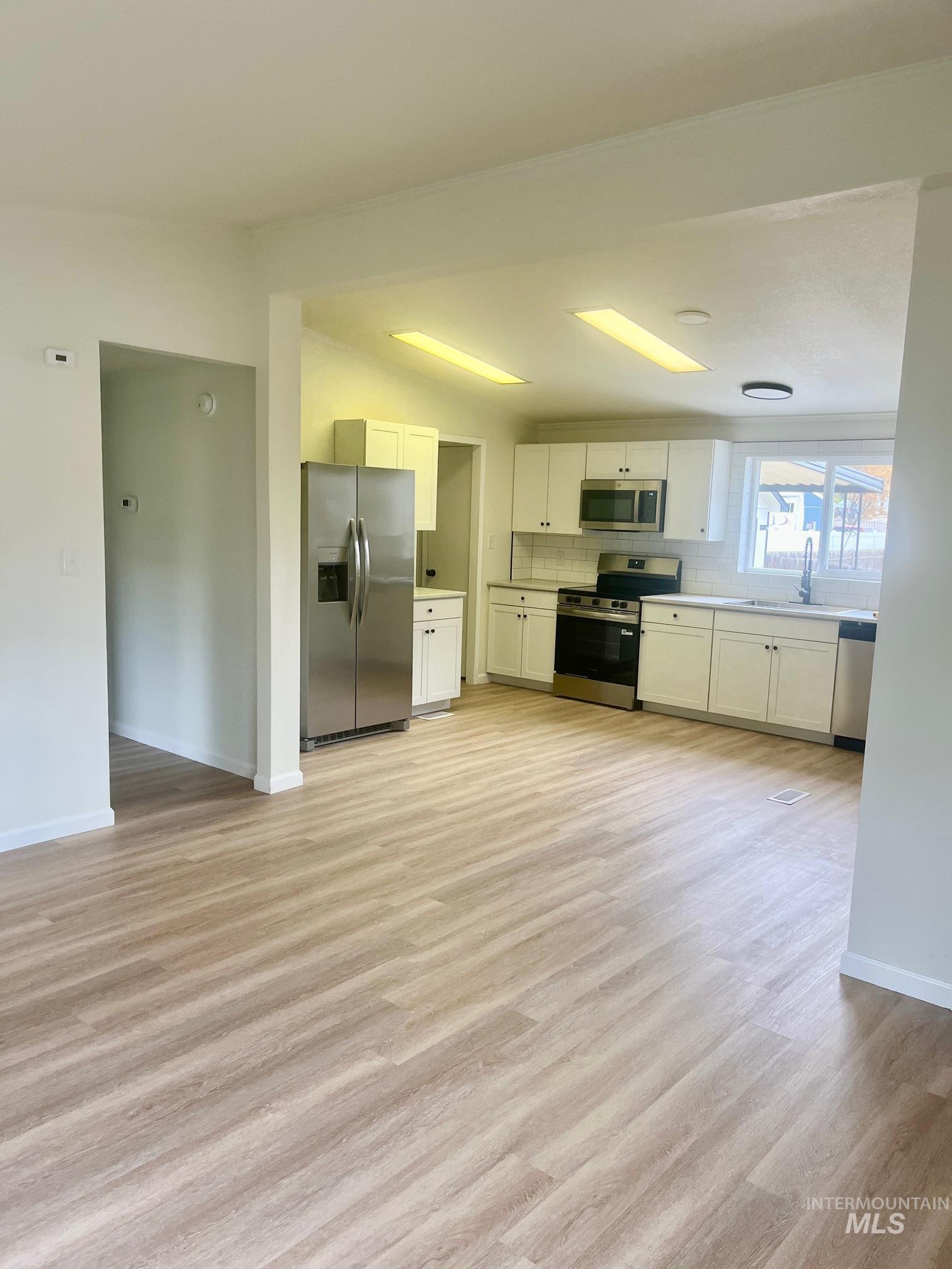 Kitchen with white cabinetry, stainless steel appliances, light wood-style floors, light countertops, and tasteful backsplash