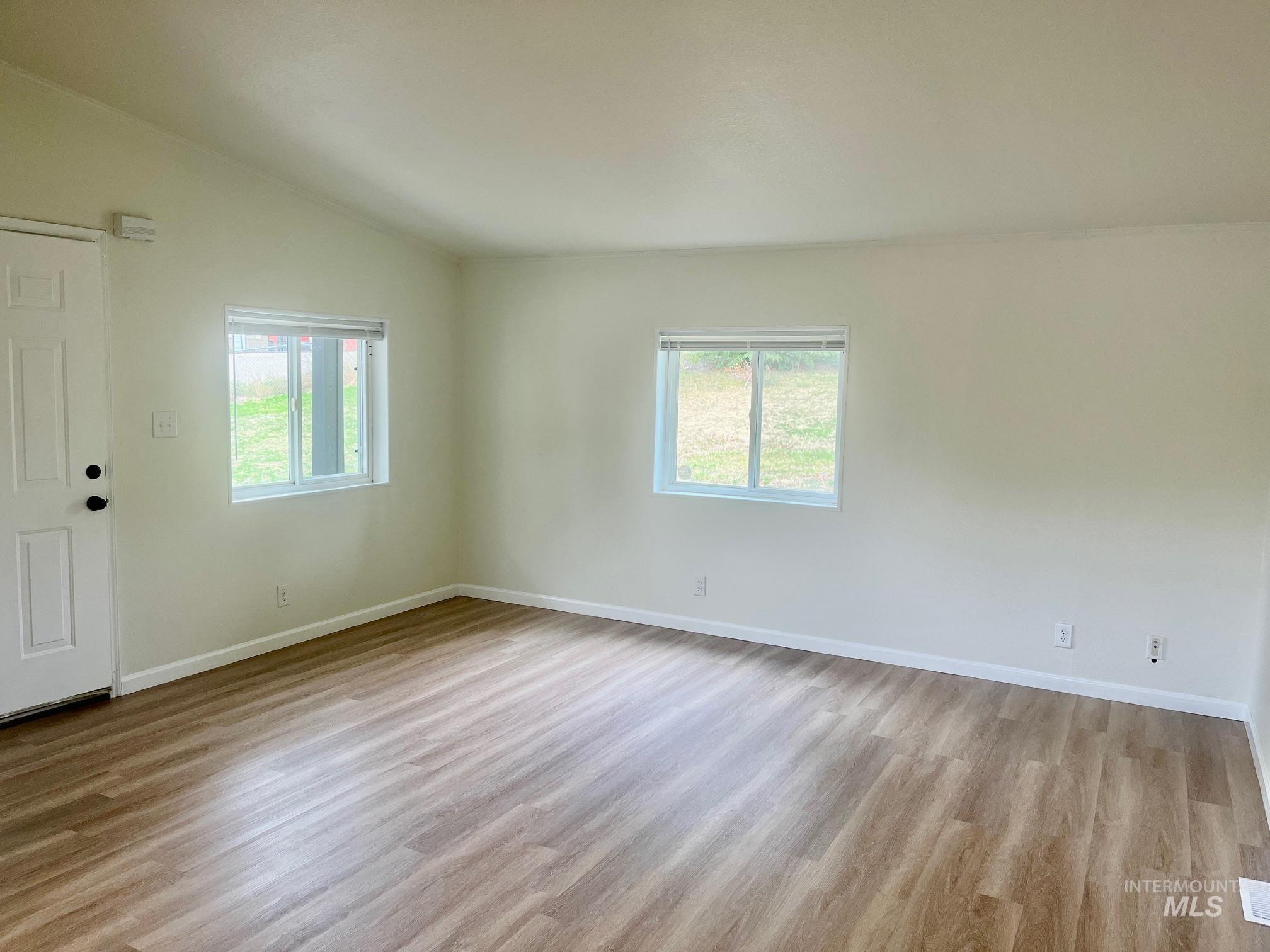 Empty room with plenty of natural light, light wood finished floors, and lofted ceiling