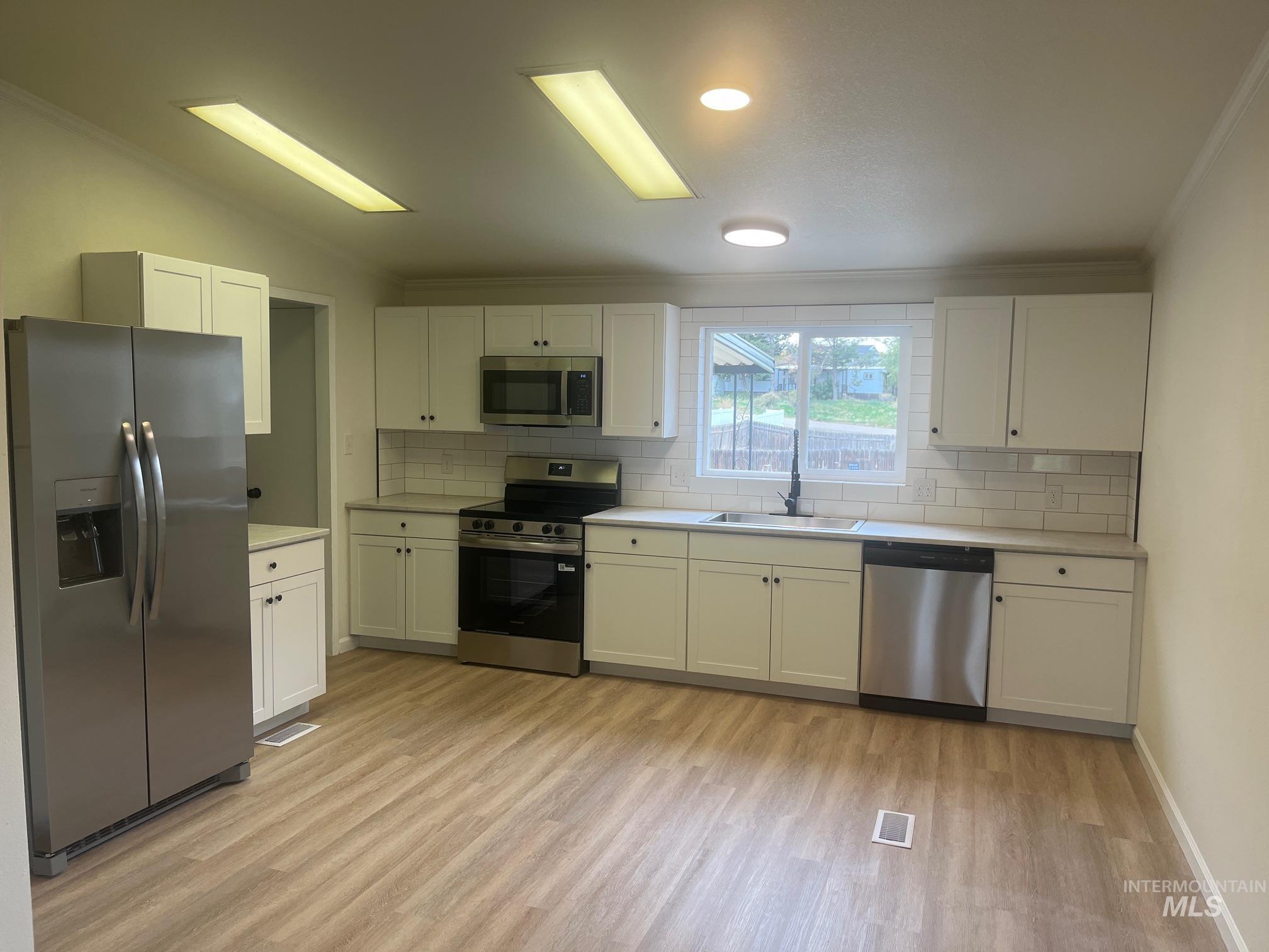 Kitchen featuring appliances with stainless steel finishes, light countertops, tasteful backsplash, white cabinets, and light wood-style flooring