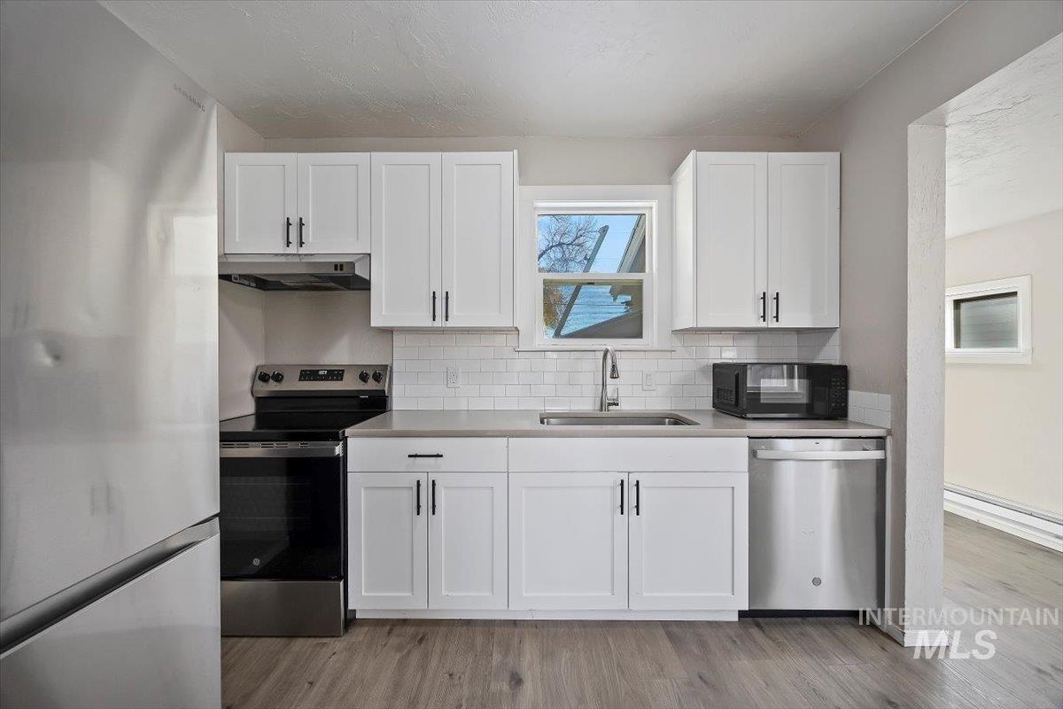 Kitchen with appliances with stainless steel finishes, white cabinetry, backsplash, and light wood-style floors