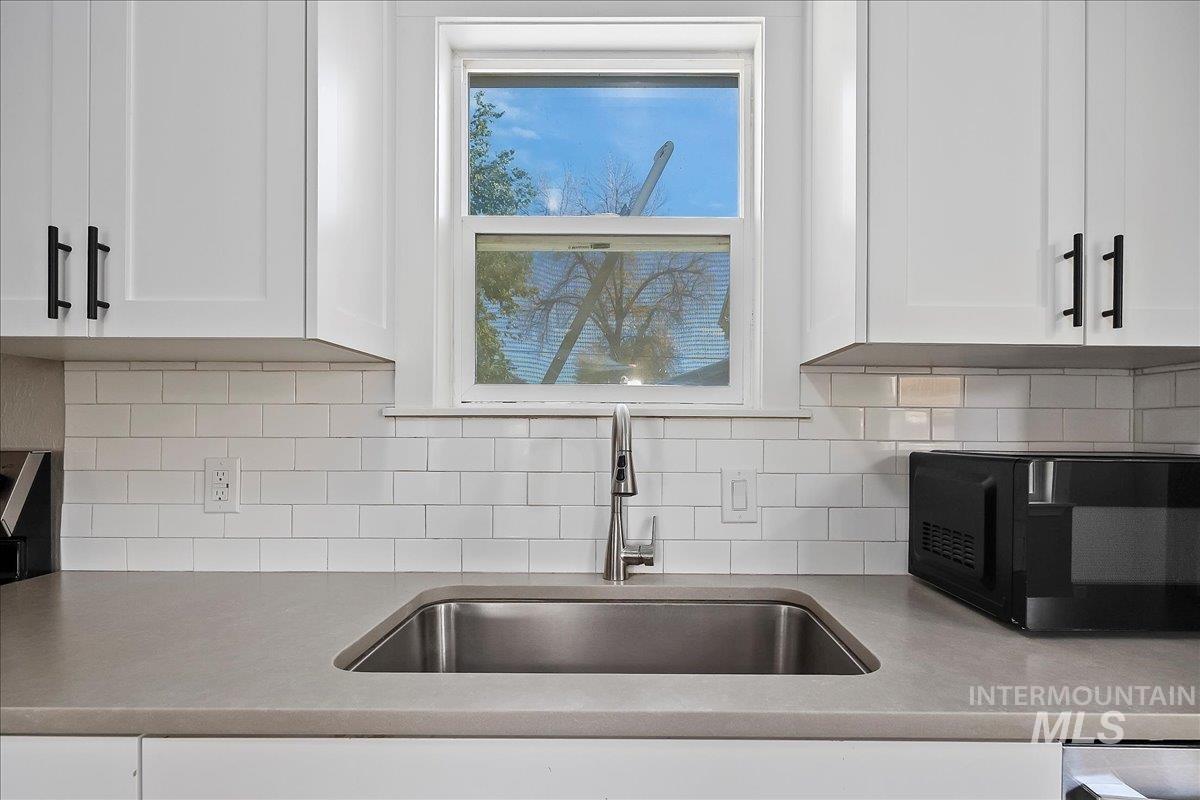 Kitchen with white cabinetry, backsplash, and light stone counters