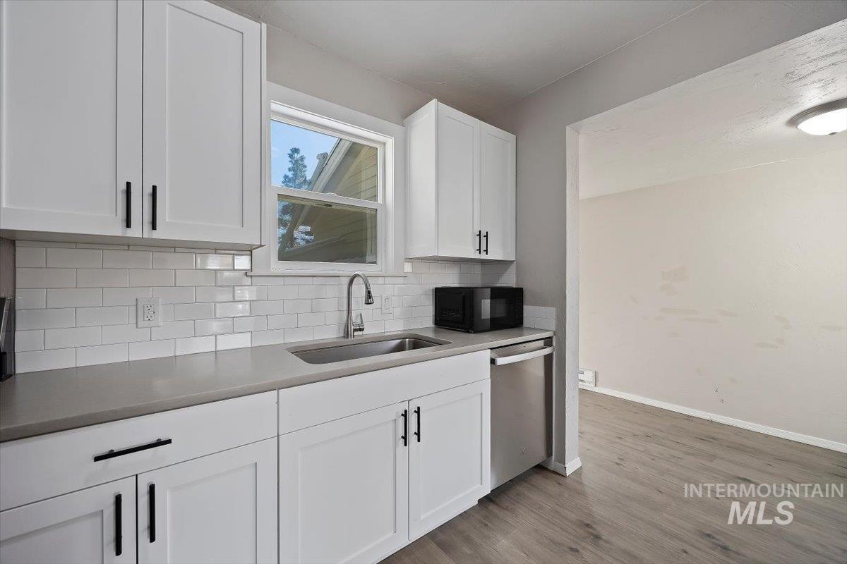Kitchen featuring white cabinets, black microwave, light wood-type flooring, tasteful backsplash, and dishwasher
