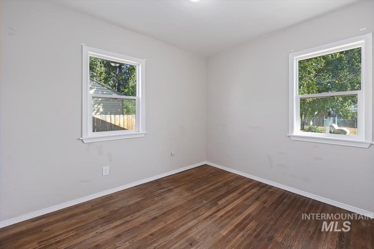 Unfurnished room with baseboards and dark wood-type flooring