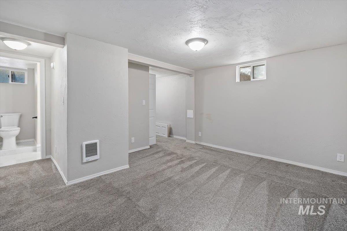 Below grade area with a textured ceiling, carpet floors, and heating unit