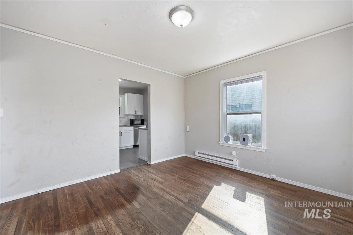 Empty room with ornamental molding, baseboard heating, and dark wood-type flooring