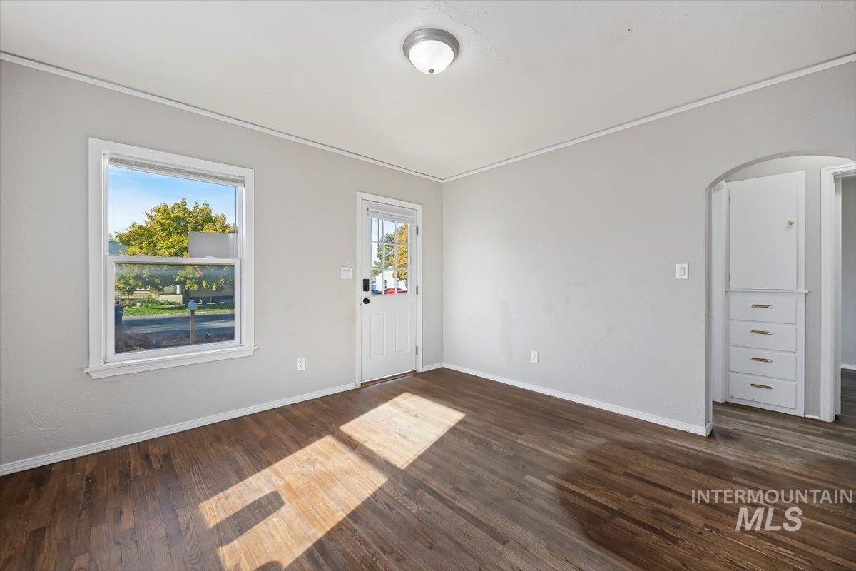 Foyer entrance with dark wood-type flooring, crown molding, and arched walkways