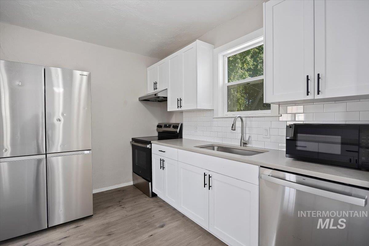 Kitchen with appliances with stainless steel finishes, light wood-type flooring, white cabinets, and tasteful backsplash