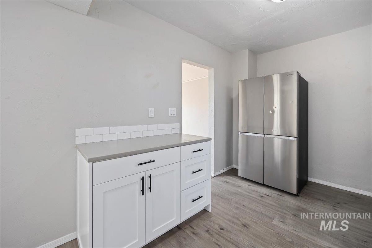 Kitchen with freestanding refrigerator, white cabinets, light wood finished floors, and light countertops