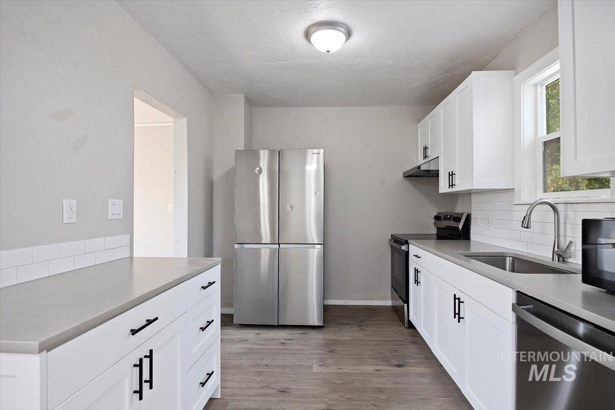 Kitchen featuring appliances with stainless steel finishes, white cabinets, backsplash, light wood-style flooring, and light countertops