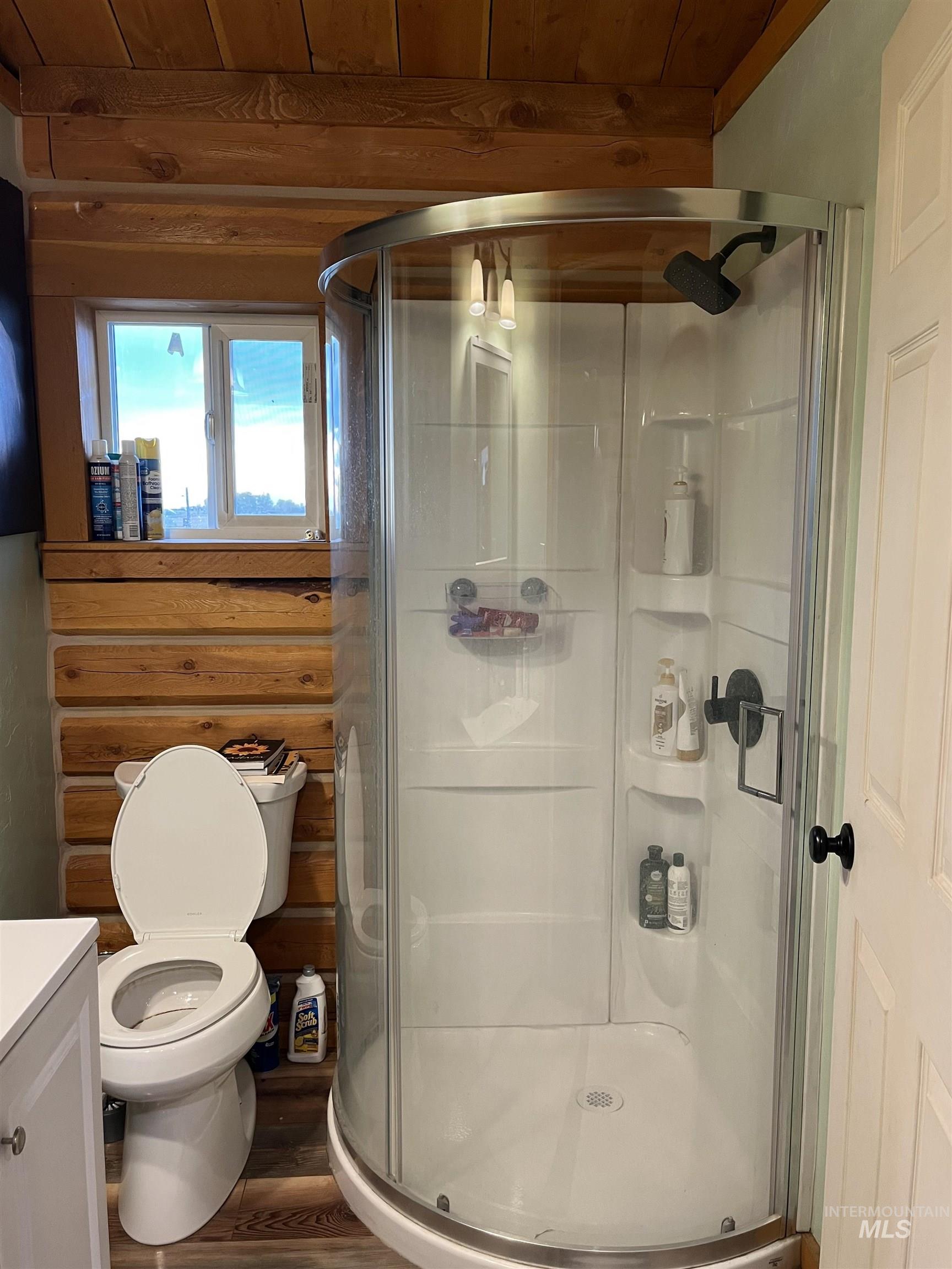 Full bathroom with vanity, a shower stall, wood finished floors, rustic walls, and wood ceiling