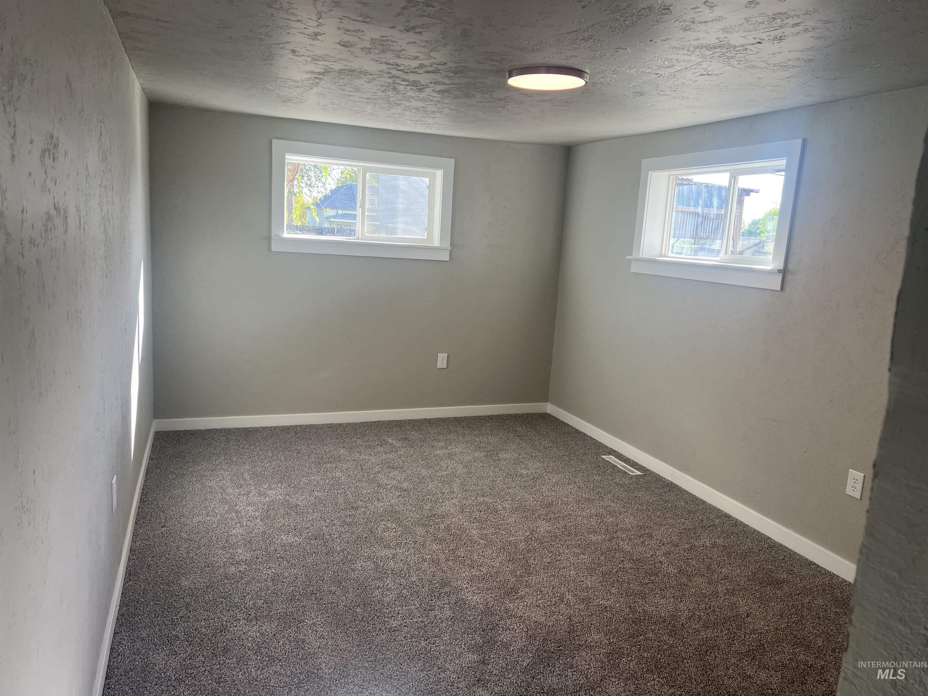 Carpeted empty room featuring a textured ceiling and a textured wall