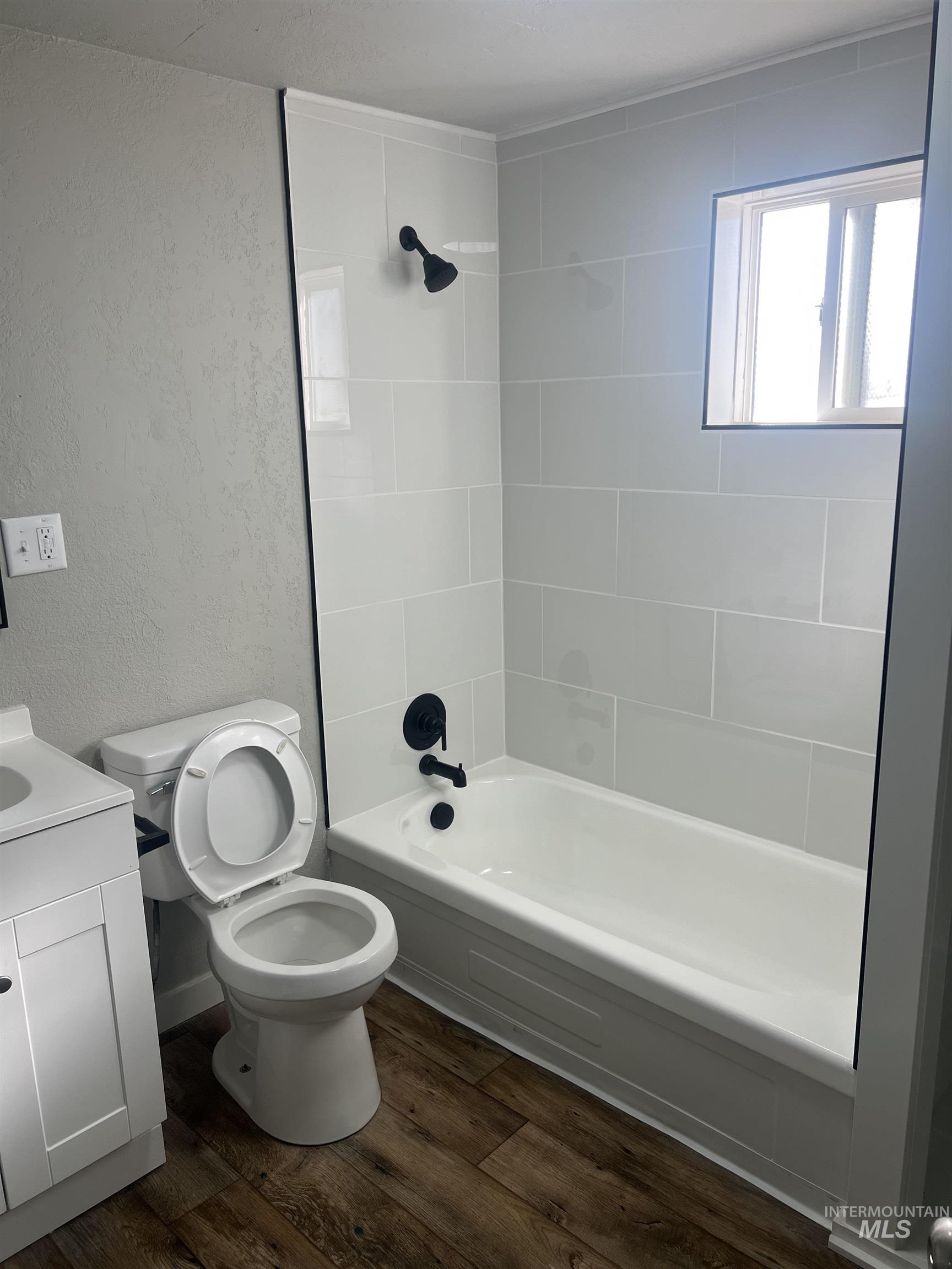 Full bath with a textured wall, shower / bathtub combination, dark wood finished floors, and vanity