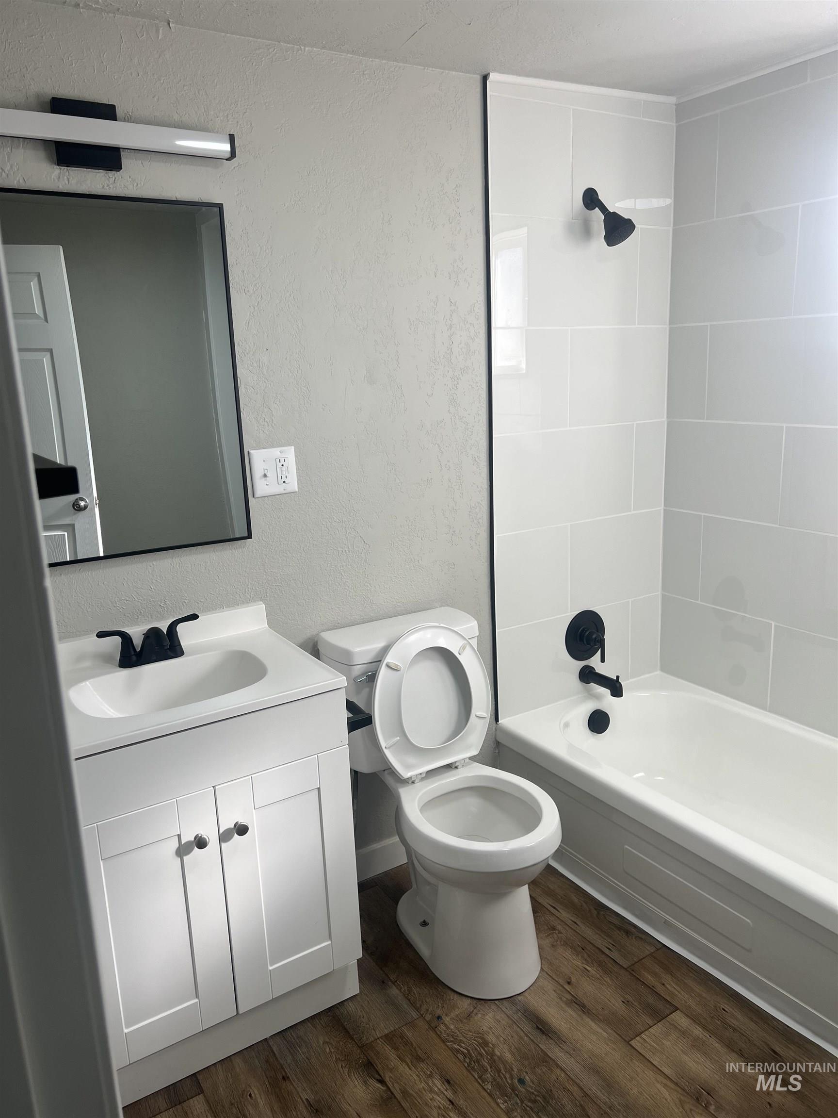 Bathroom featuring a textured wall, dark wood-style flooring, bathing tub / shower combination, and vanity
