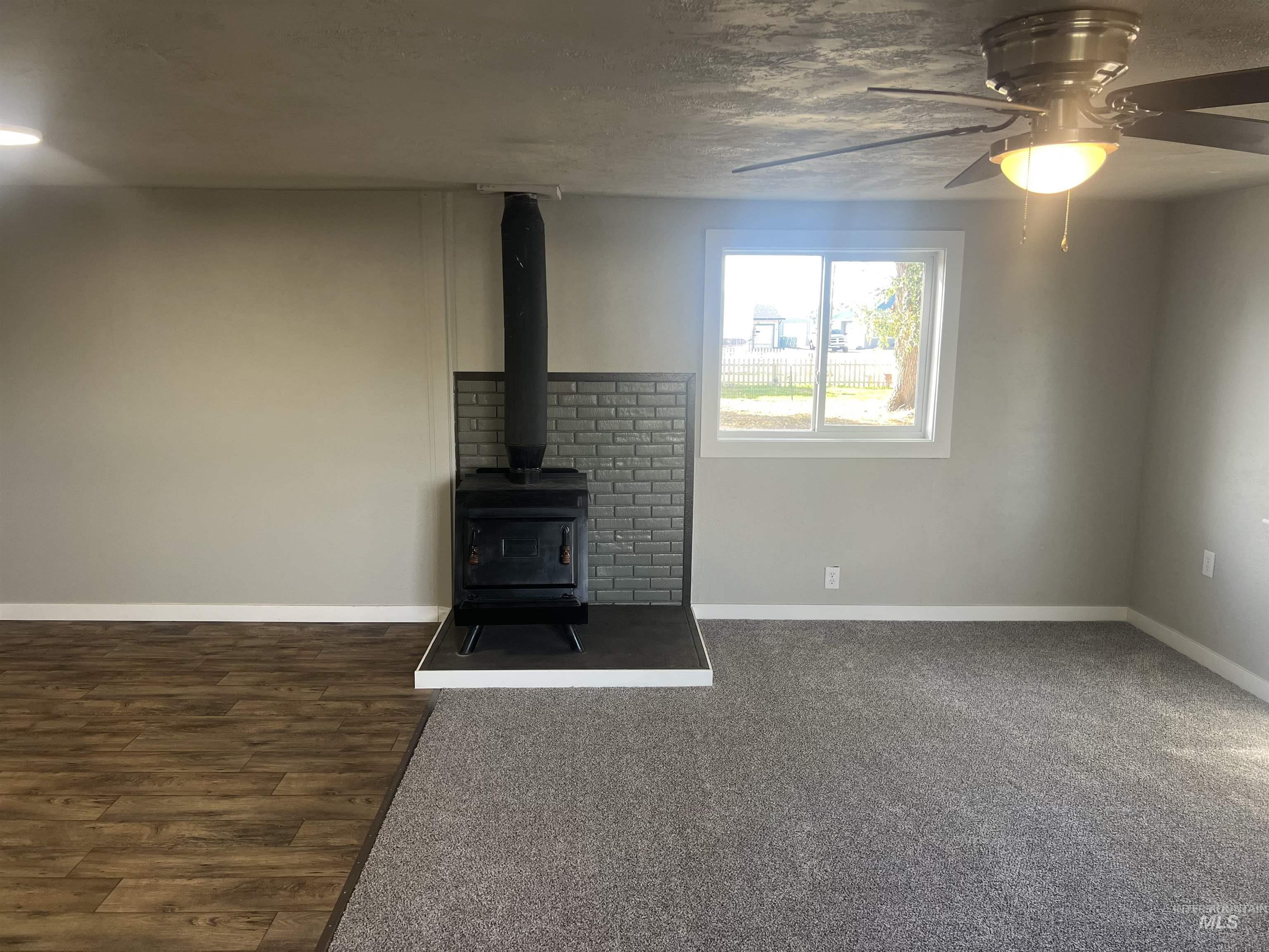 Unfurnished living room featuring a wood stove, a ceiling fan, and a textured ceiling