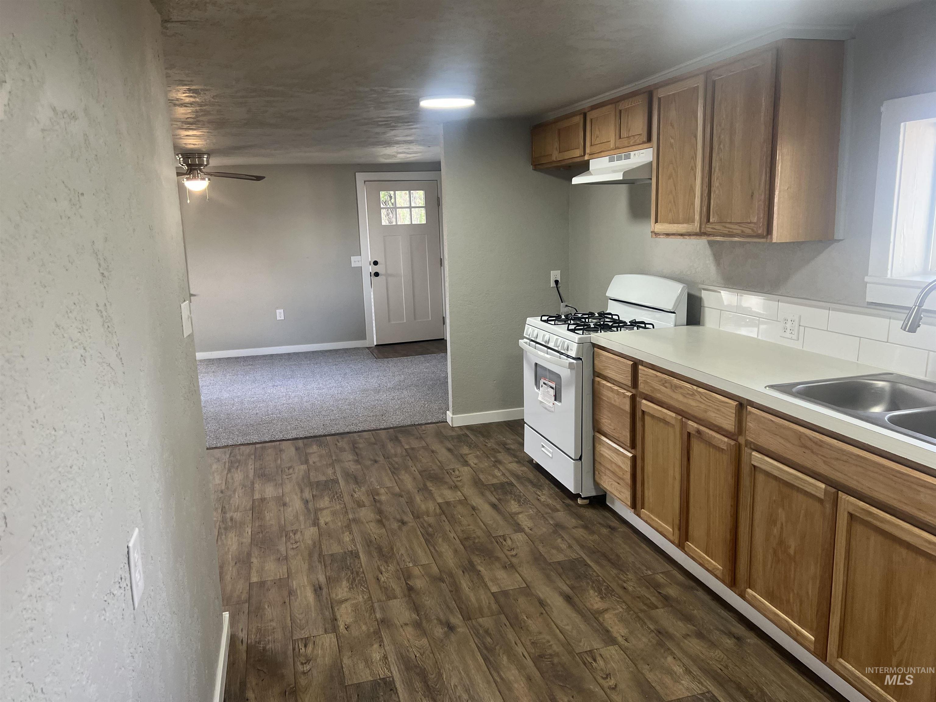 Kitchen featuring gas range gas stove, light countertops, dark wood-style floors, brown cabinetry, and a ceiling fan