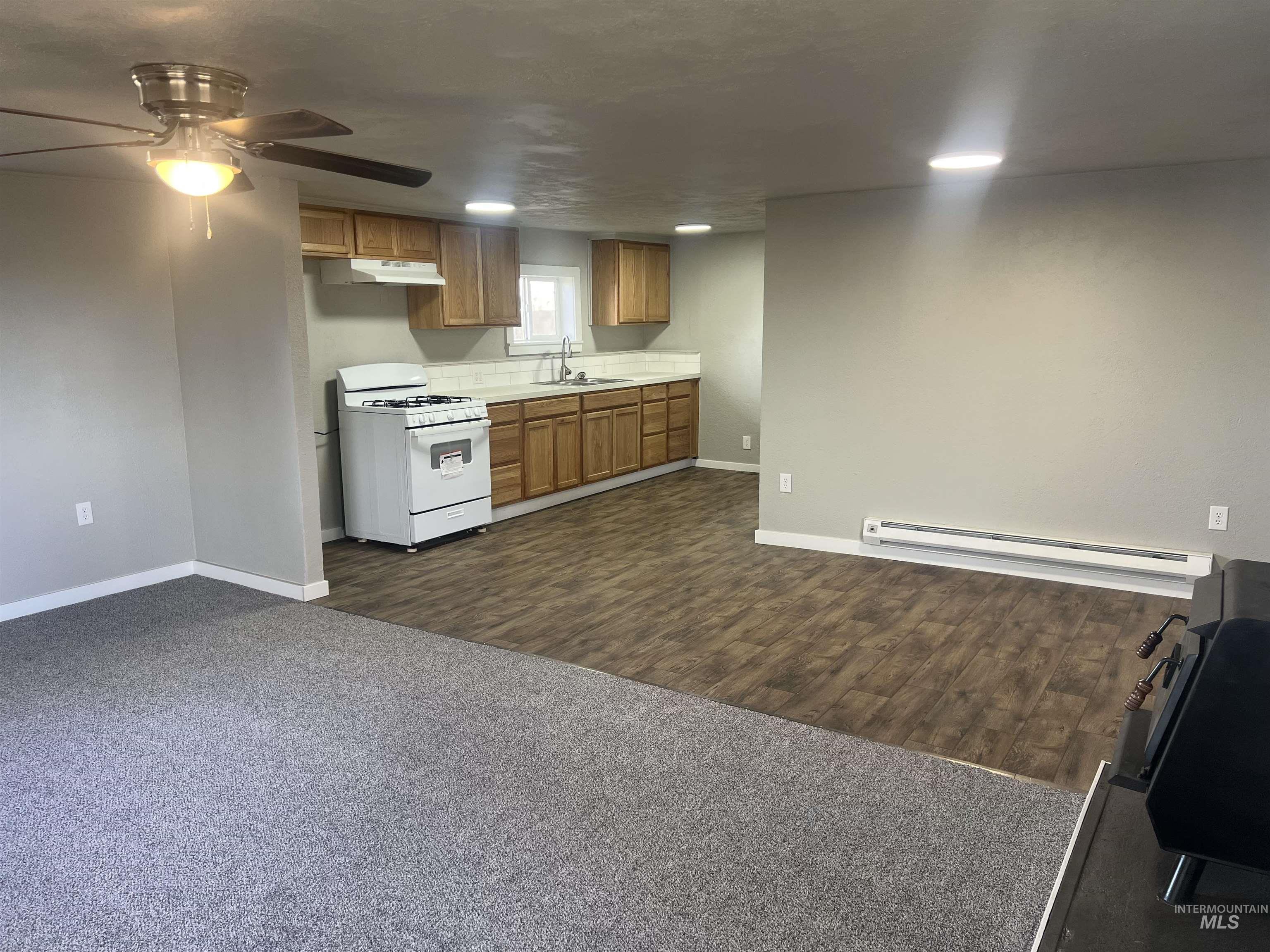 Kitchen with white range with gas stovetop, light countertops, baseboard heating, brown cabinets, and dark carpet