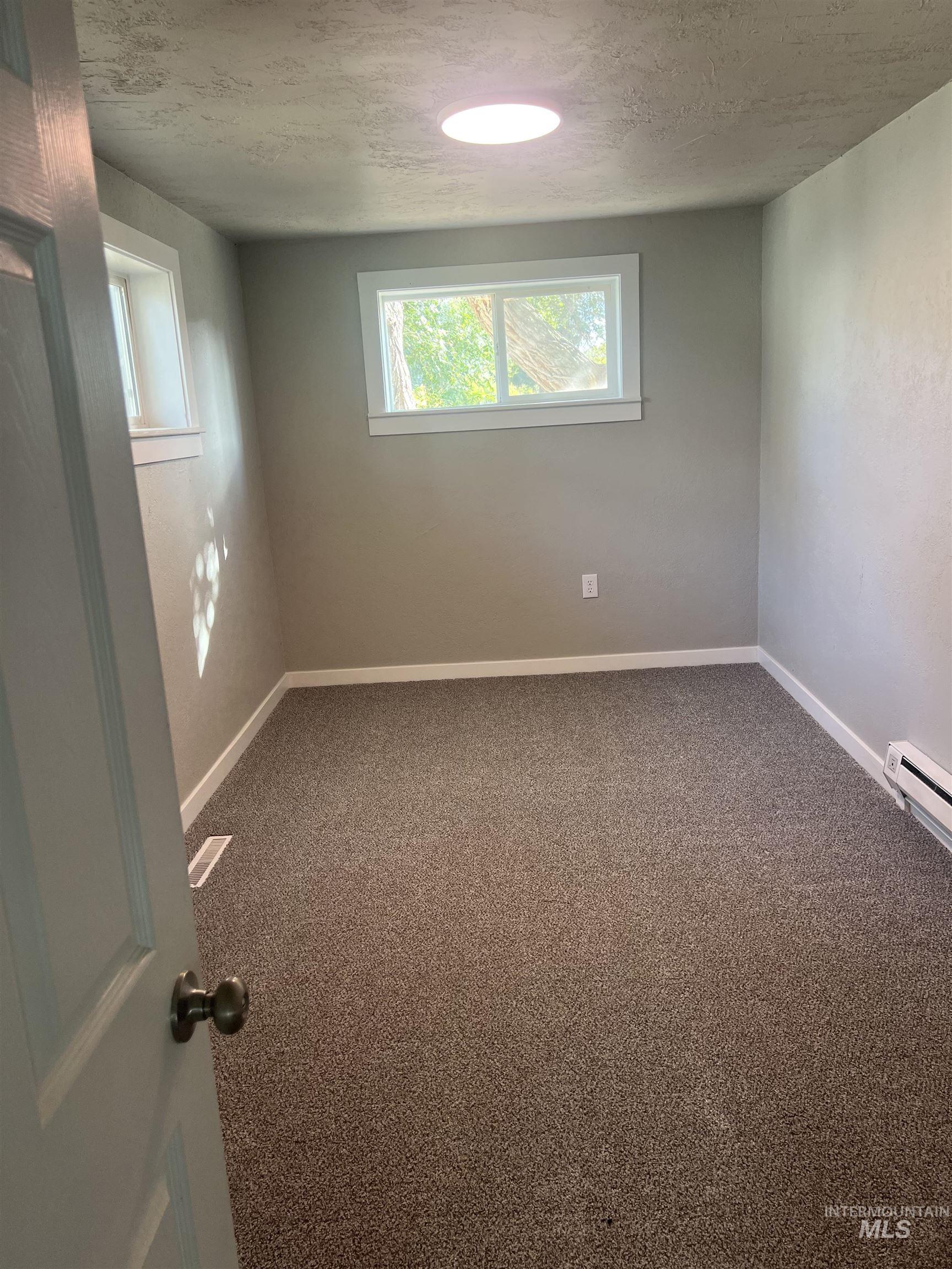 Empty room with carpet, a textured ceiling, and a baseboard radiator