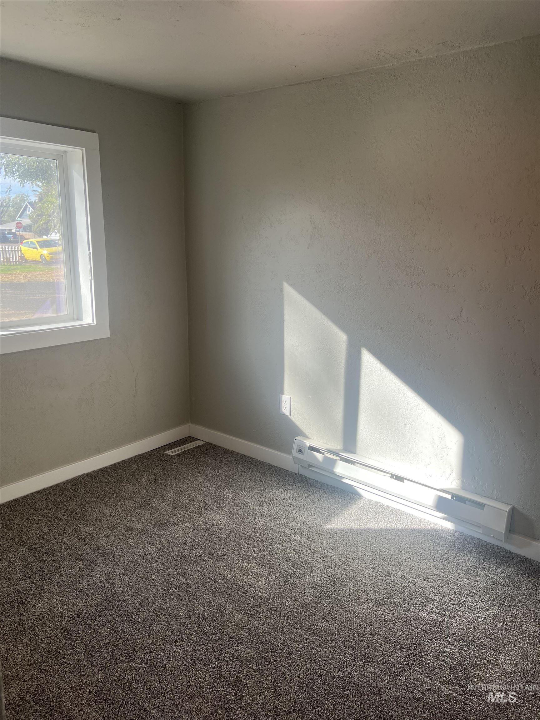 Carpeted empty room with a baseboard heating unit and baseboards