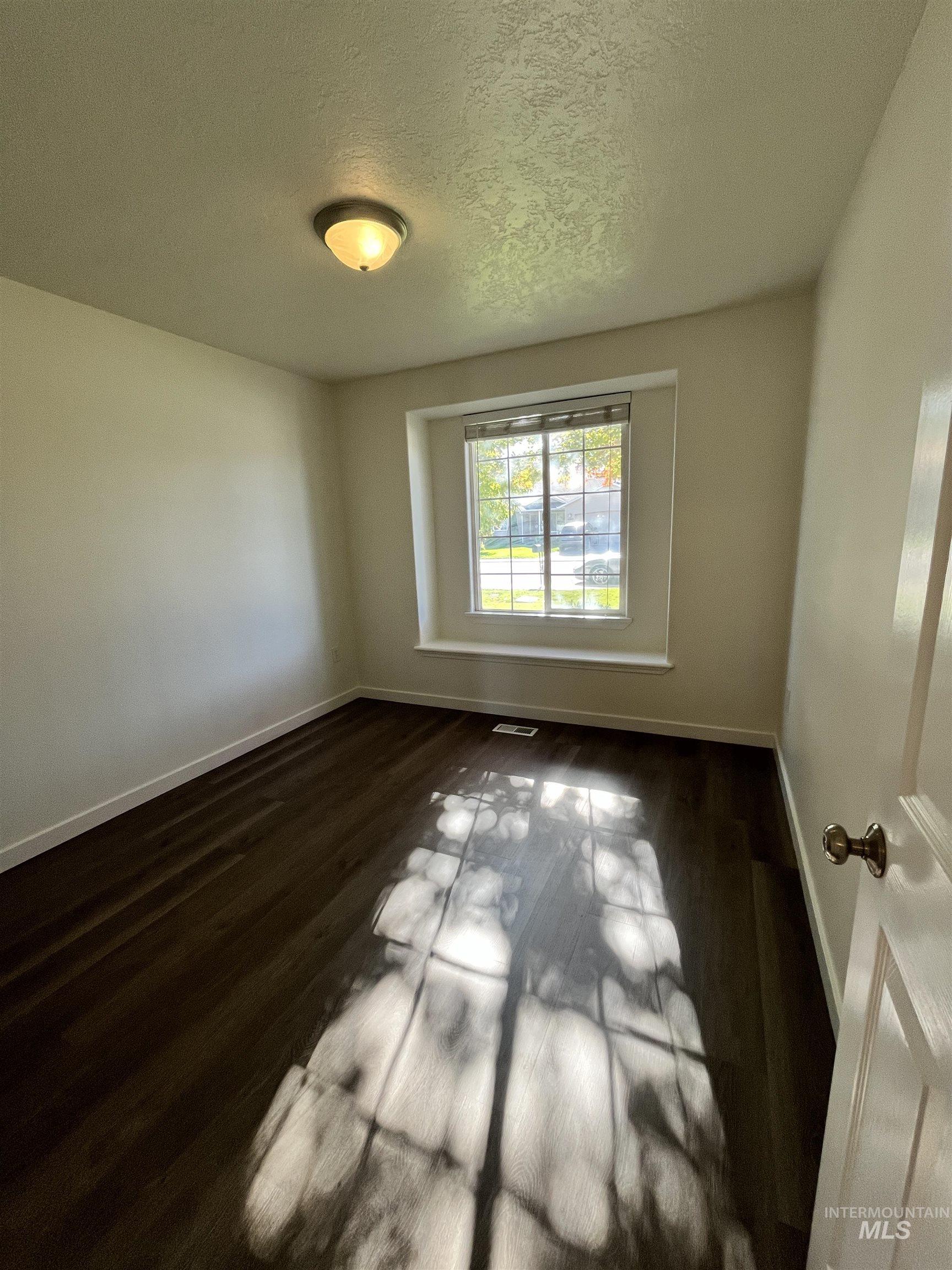 Empty room with a textured ceiling and dark wood-type flooring