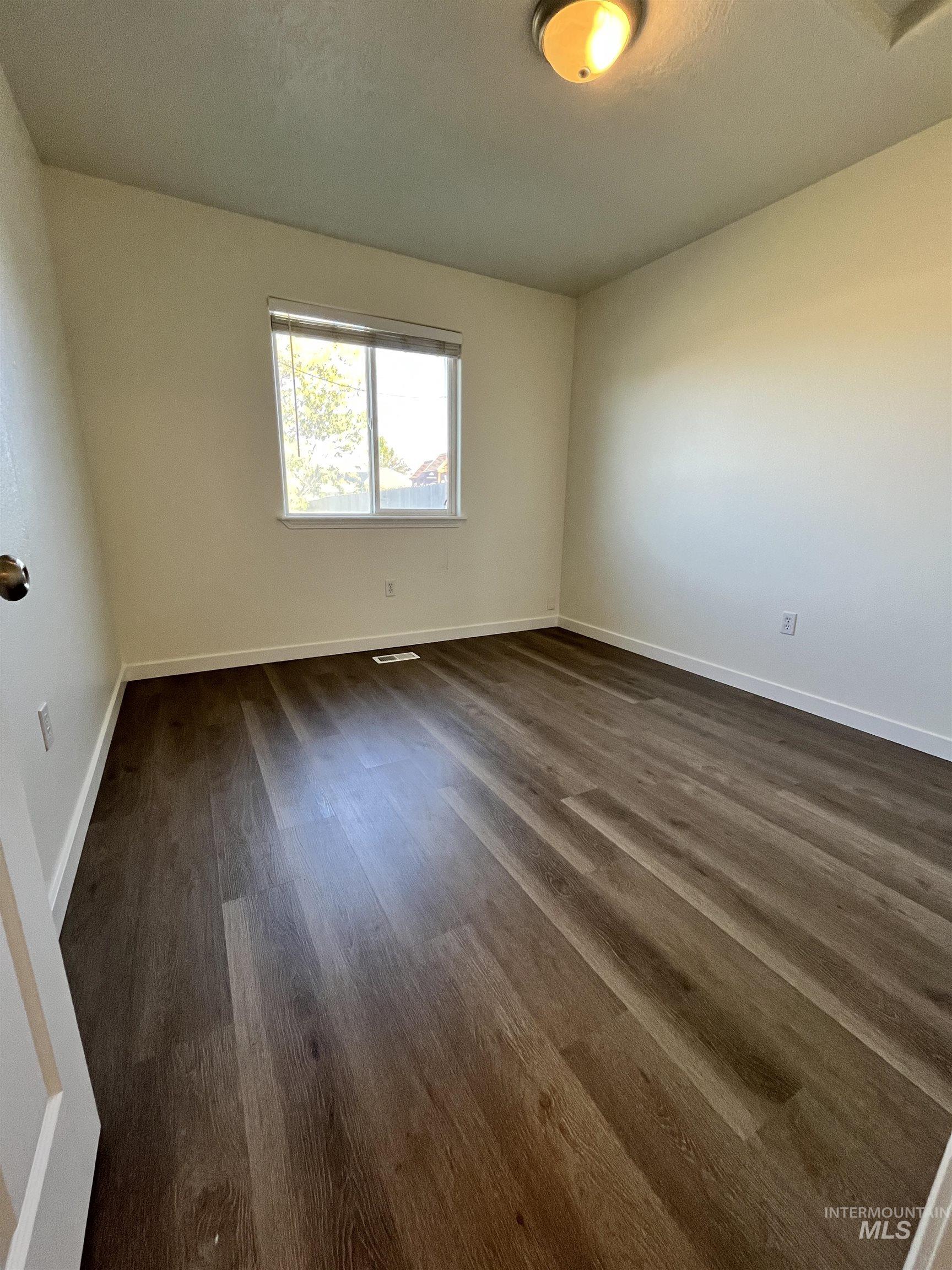 Empty room featuring baseboards and dark wood finished floors