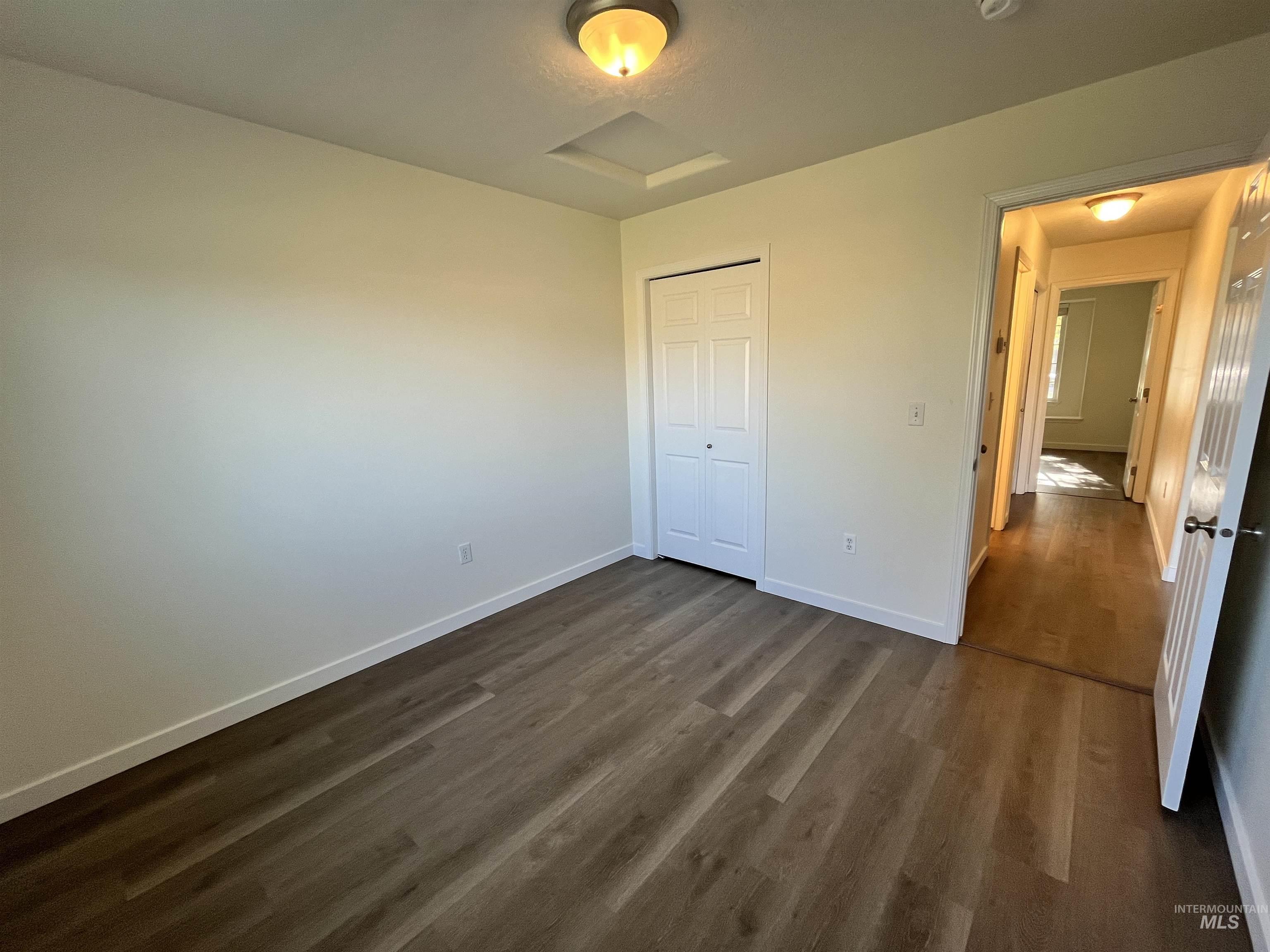 Unfurnished bedroom with attic access, dark wood finished floors, and a closet