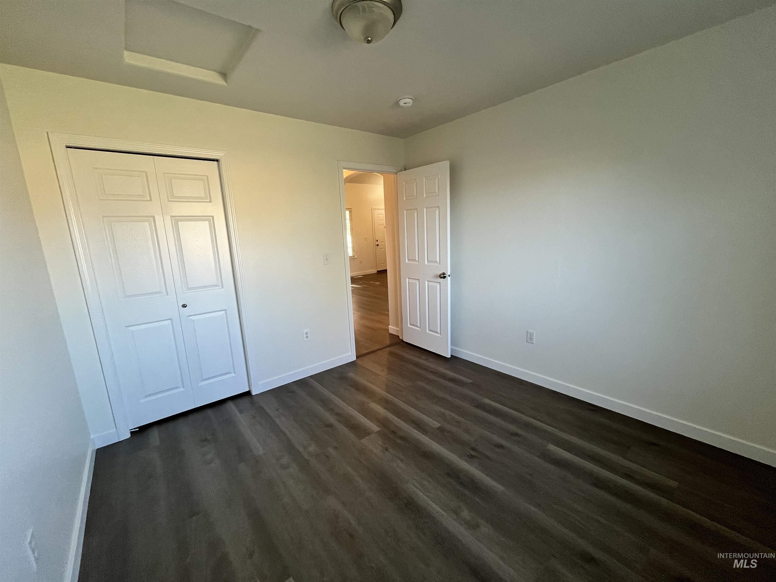 Unfurnished bedroom featuring dark wood-style flooring, attic access, a closet, and arched walkways