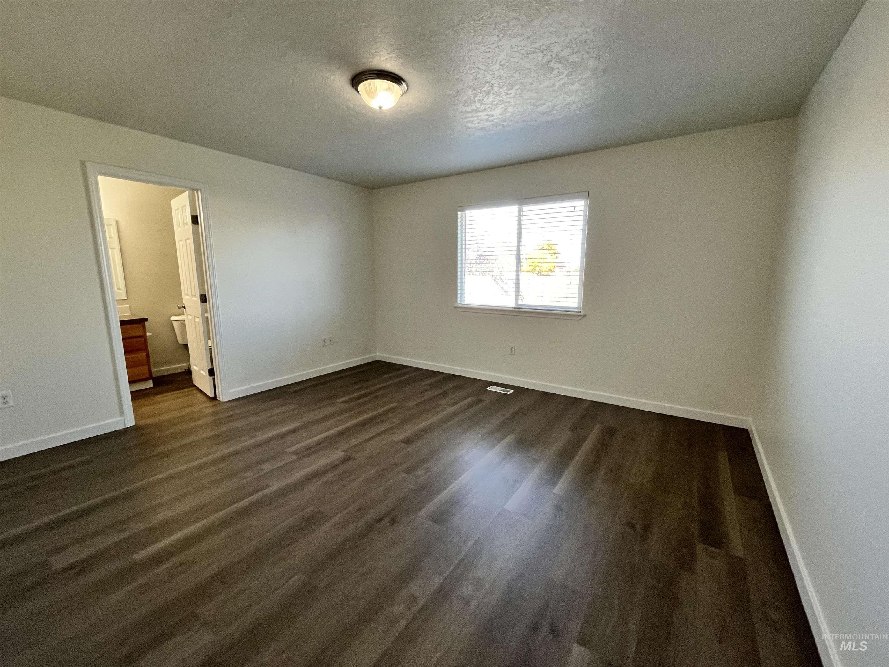 Unfurnished bedroom featuring dark wood finished floors, a textured ceiling, and ensuite bath