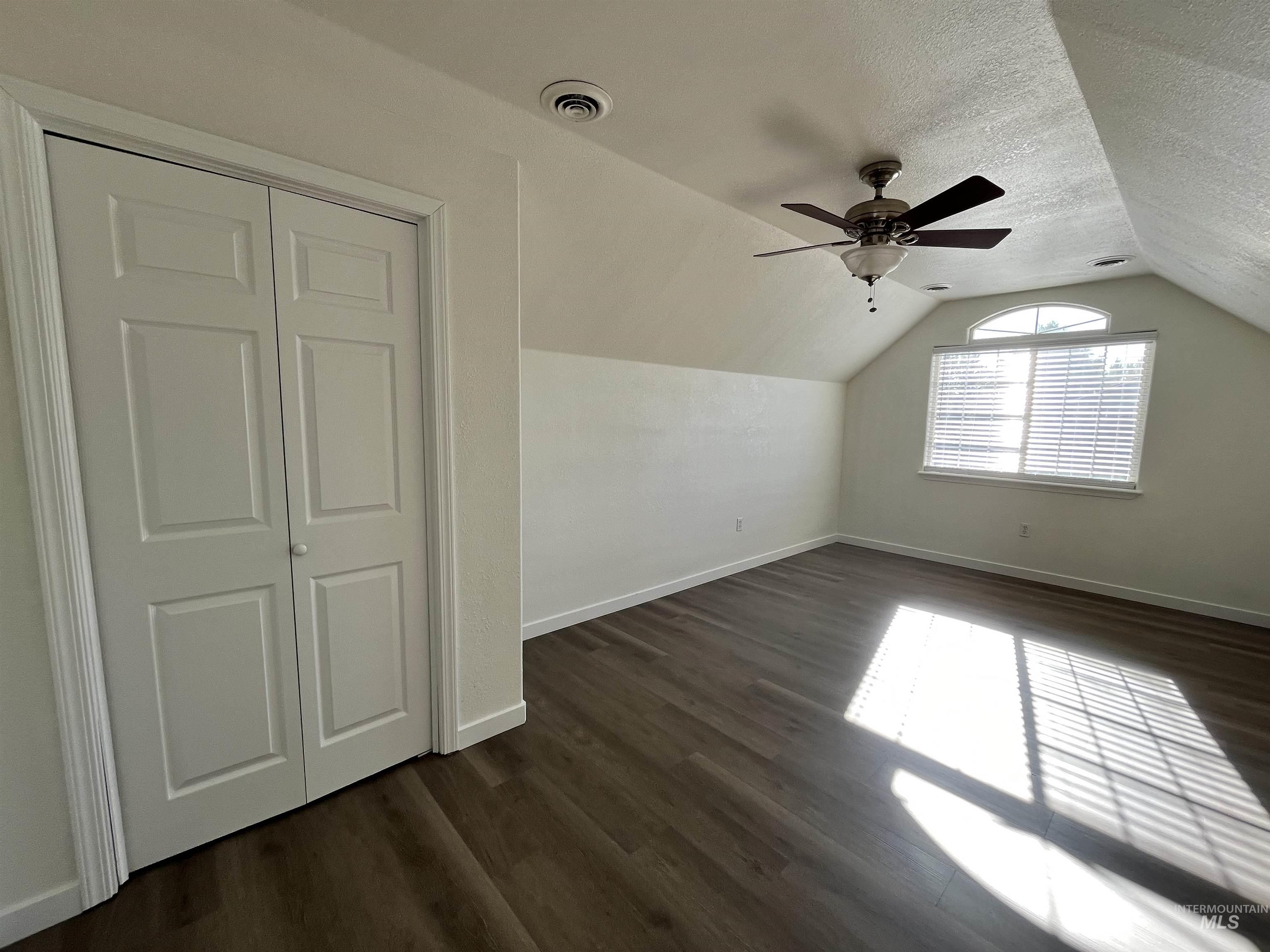 Bonus room featuring dark wood-type flooring, lofted ceiling, a textured ceiling, and a ceiling fan