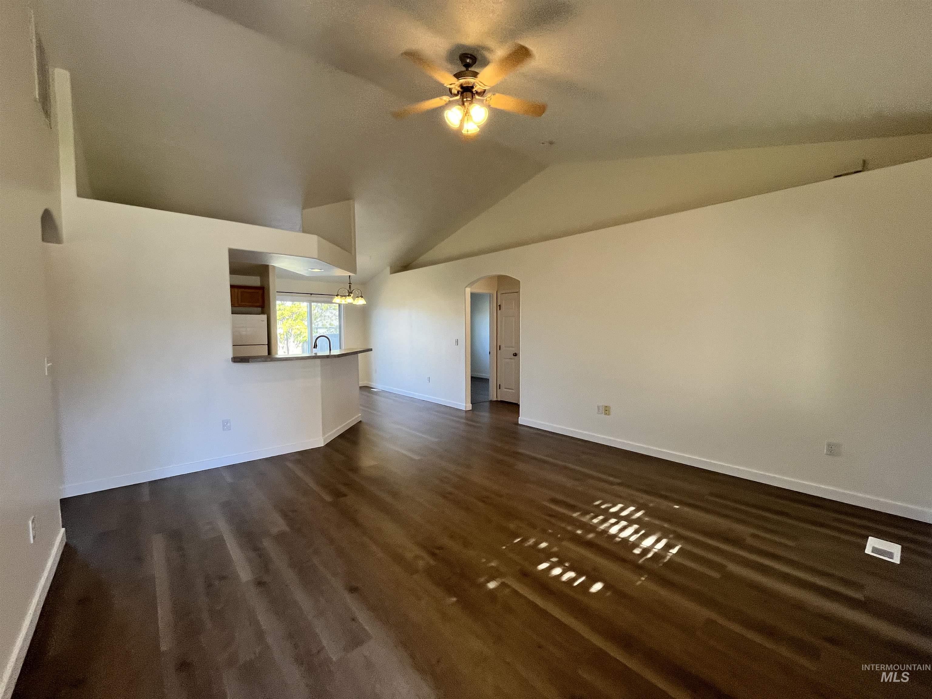 Unfurnished living room featuring arched walkways, dark wood-type flooring, lofted ceiling, and ceiling fan