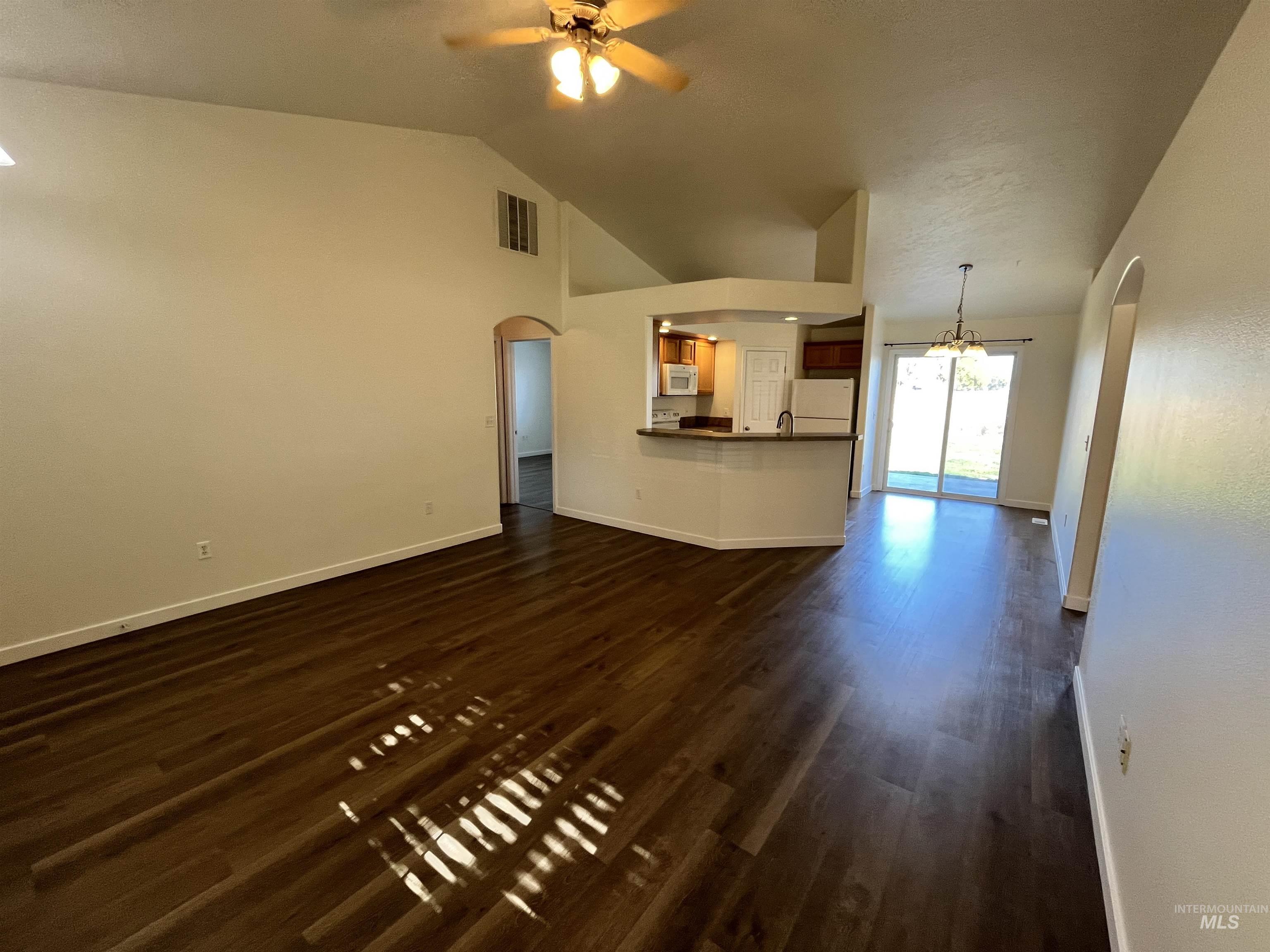 Unfurnished living room with arched walkways, dark wood finished floors, ceiling fan, a chandelier, and high vaulted ceiling