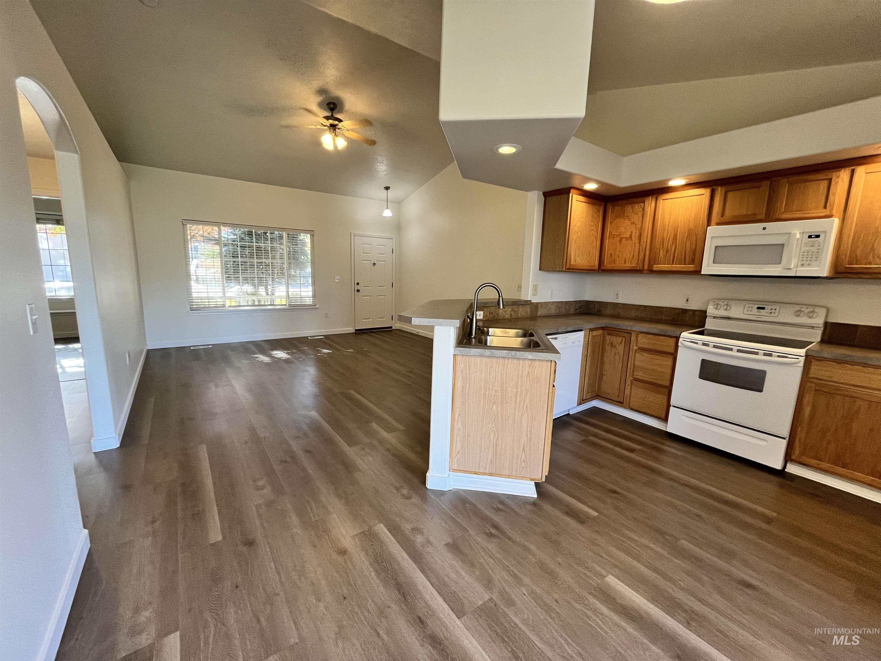 Kitchen with lofted ceiling, white appliances, open floor plan, a peninsula, and dark wood-style flooring