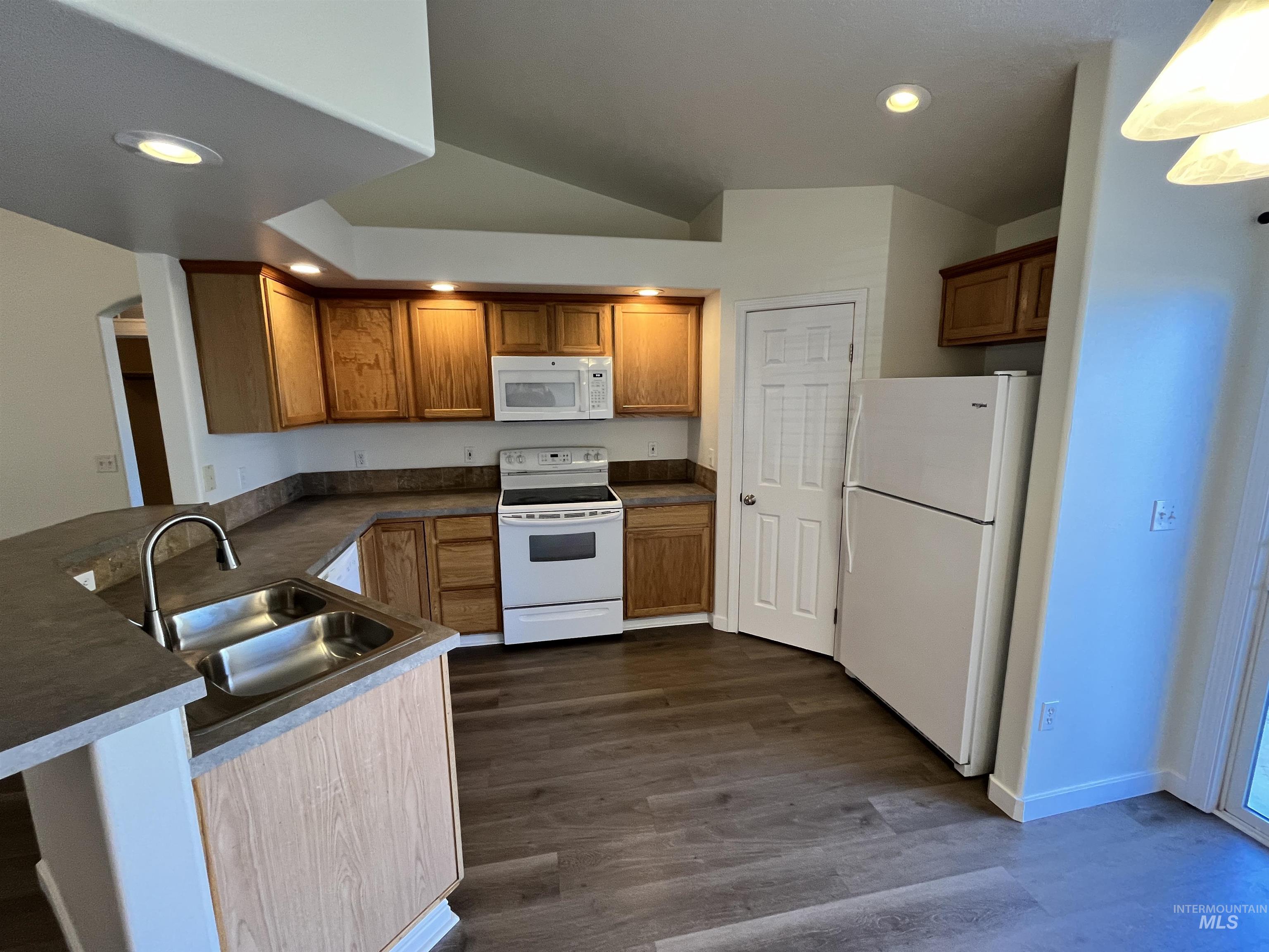 Kitchen with white appliances, dark countertops, recessed lighting, dark wood-style flooring, and brown cabinetry
