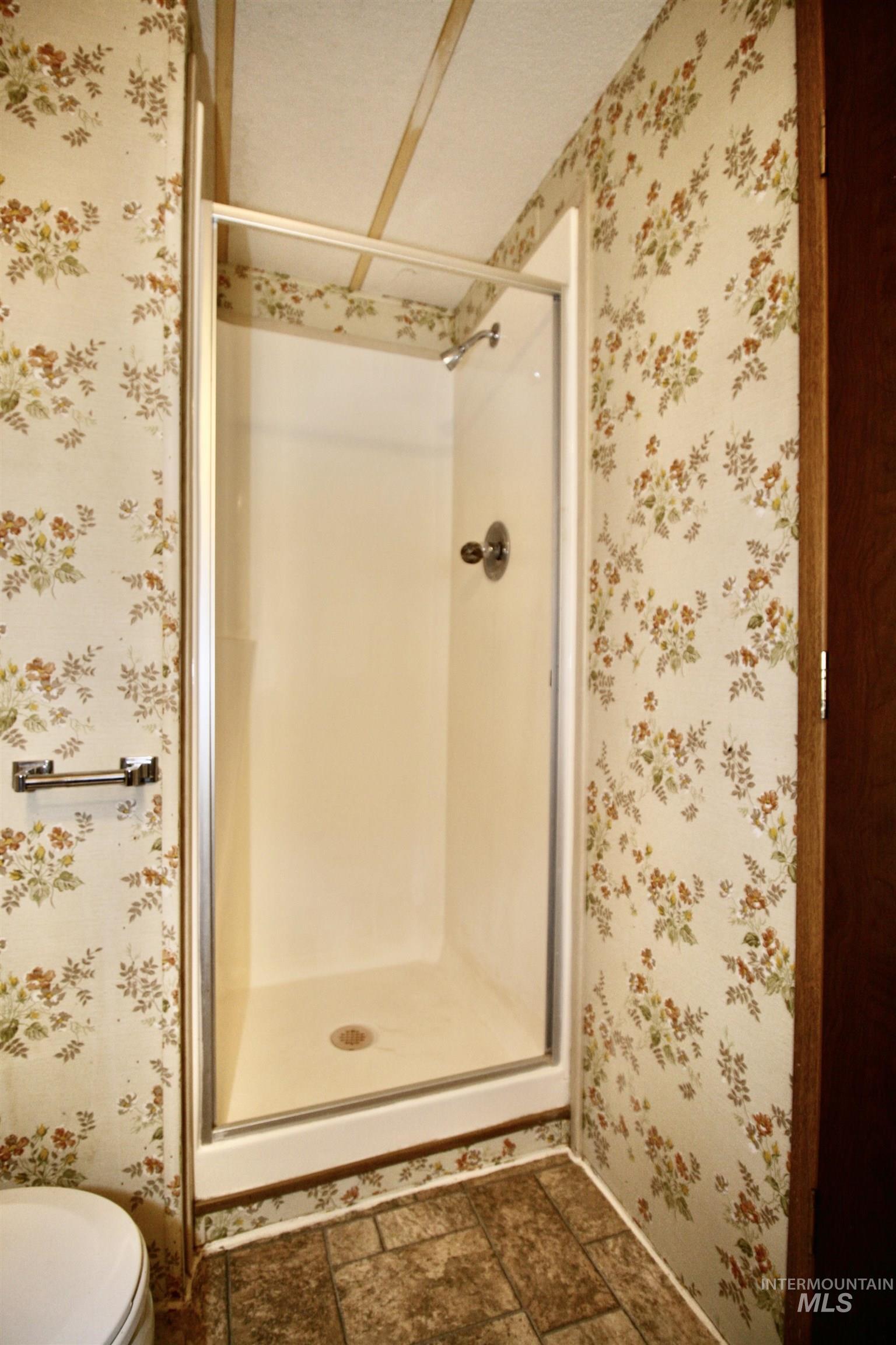 Full bathroom with a stall shower, wallpapered walls, and stone finish flooring