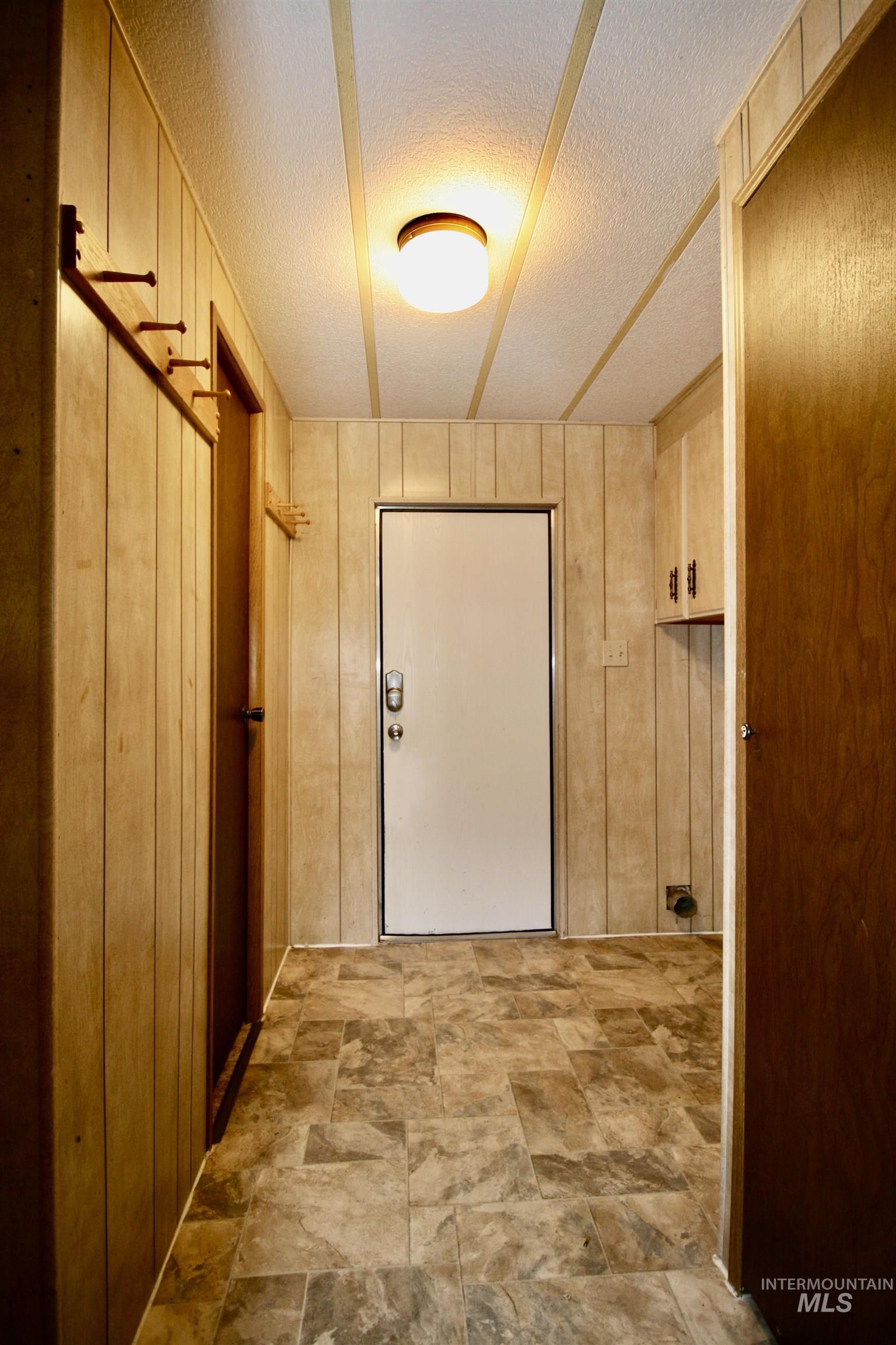 Hall featuring wood walls, a textured ceiling, and stone finish floors