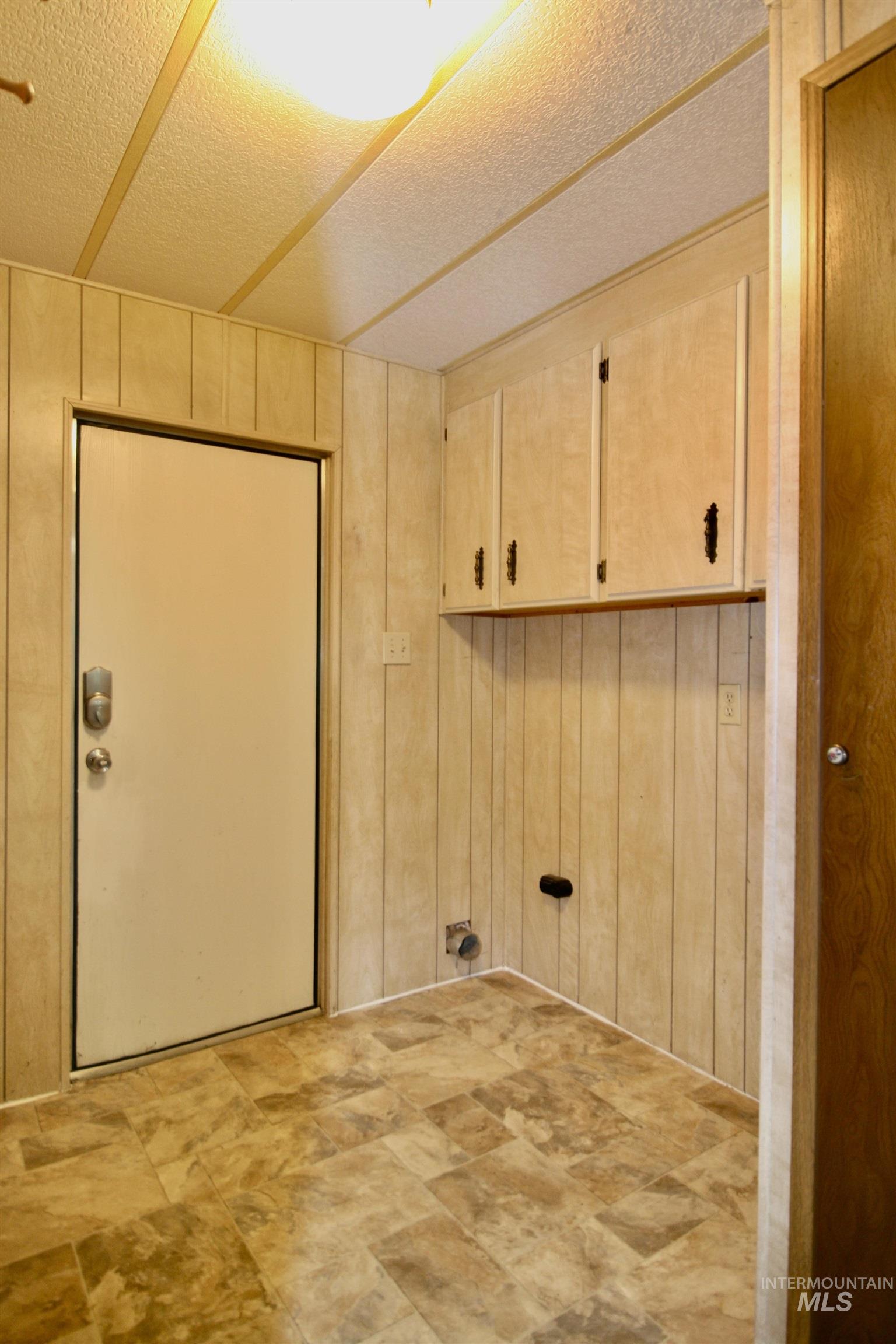 Laundry area with cabinet space, wood walls, and a textured ceiling