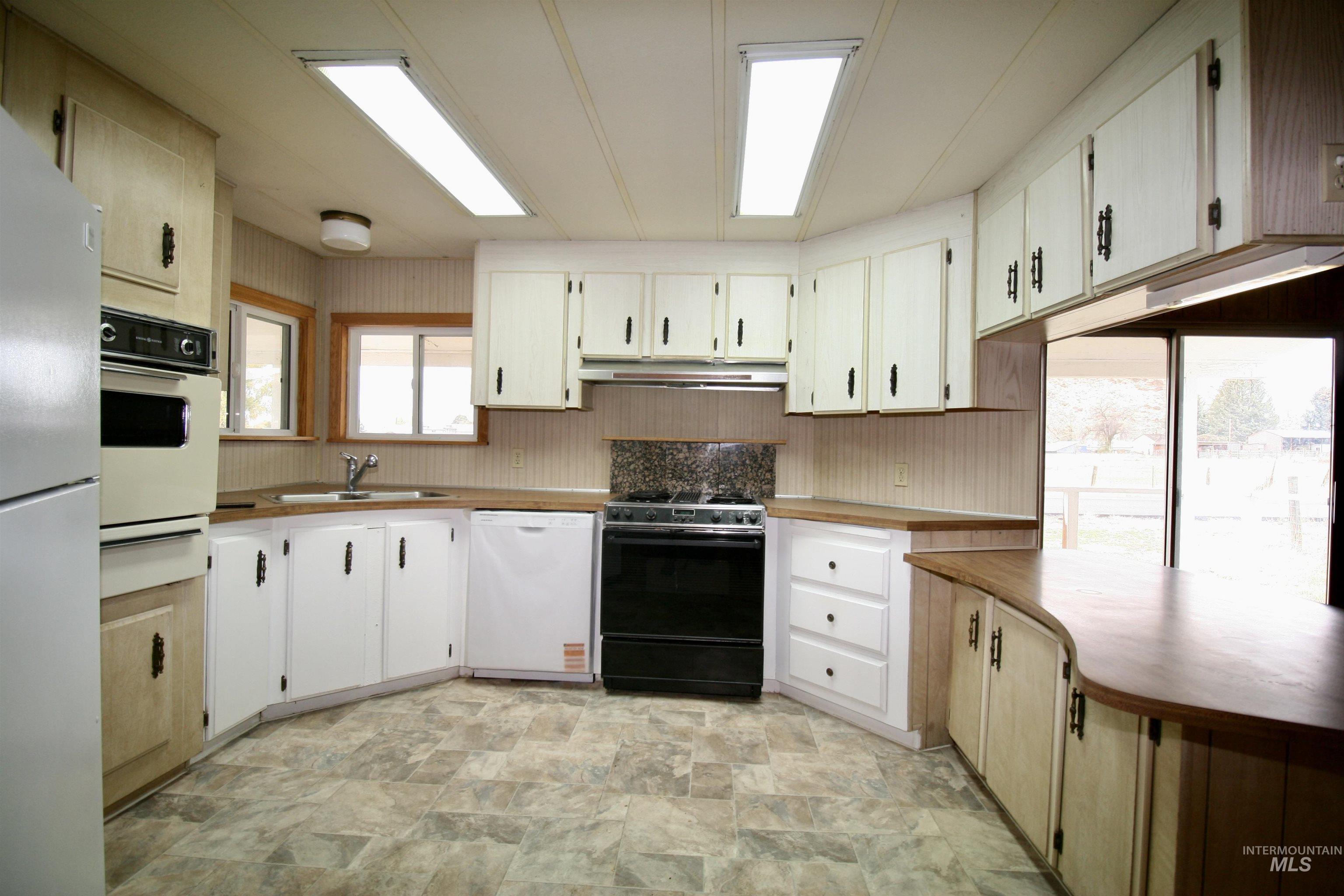 Kitchen with white appliances, stone finish flooring, a warming drawer, light countertops, and under cabinet range hood
